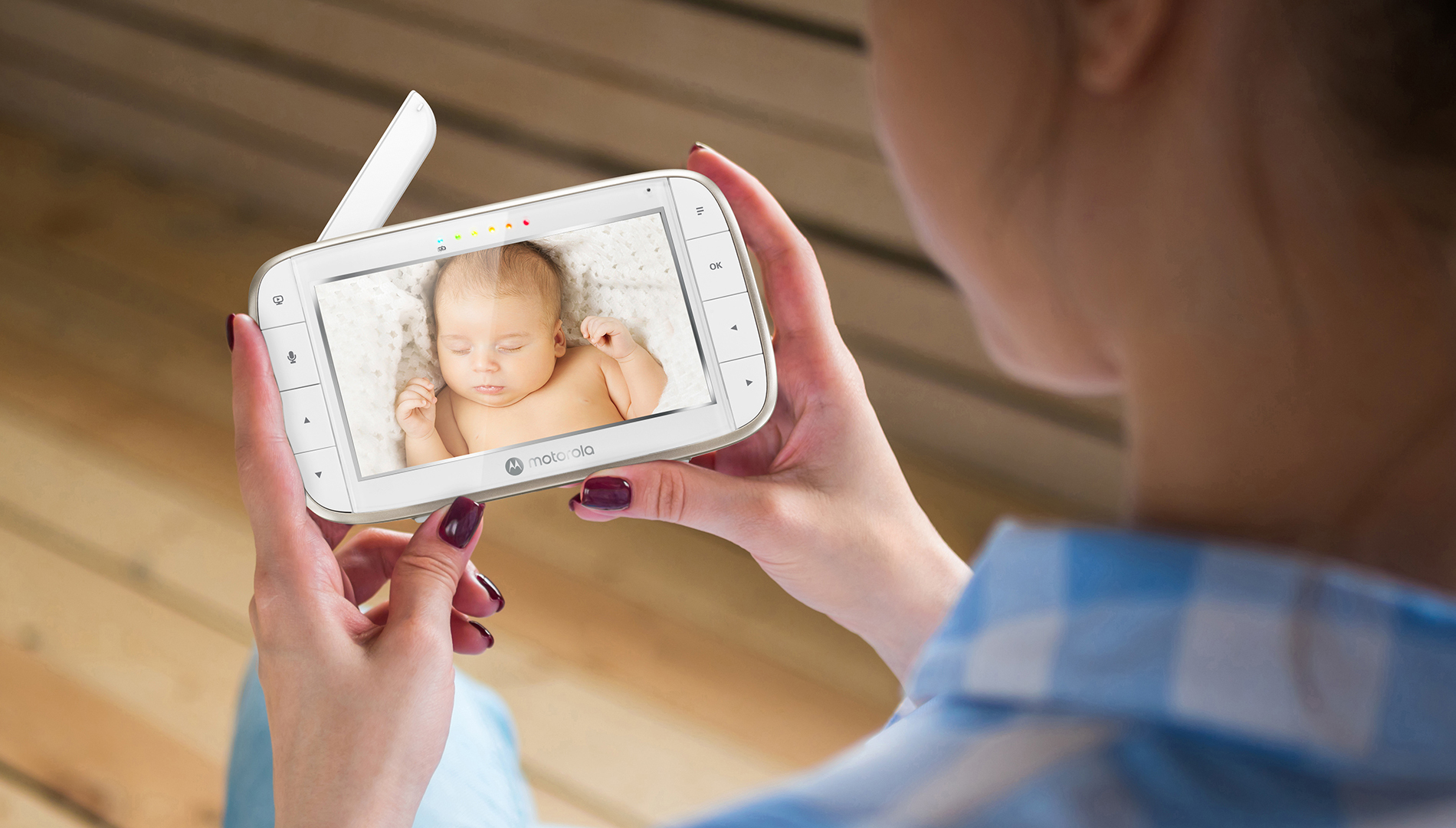 Eine Frau hält ein Babyfon, das ein schlafendes Baby auf einer weißen Decke zeigt.