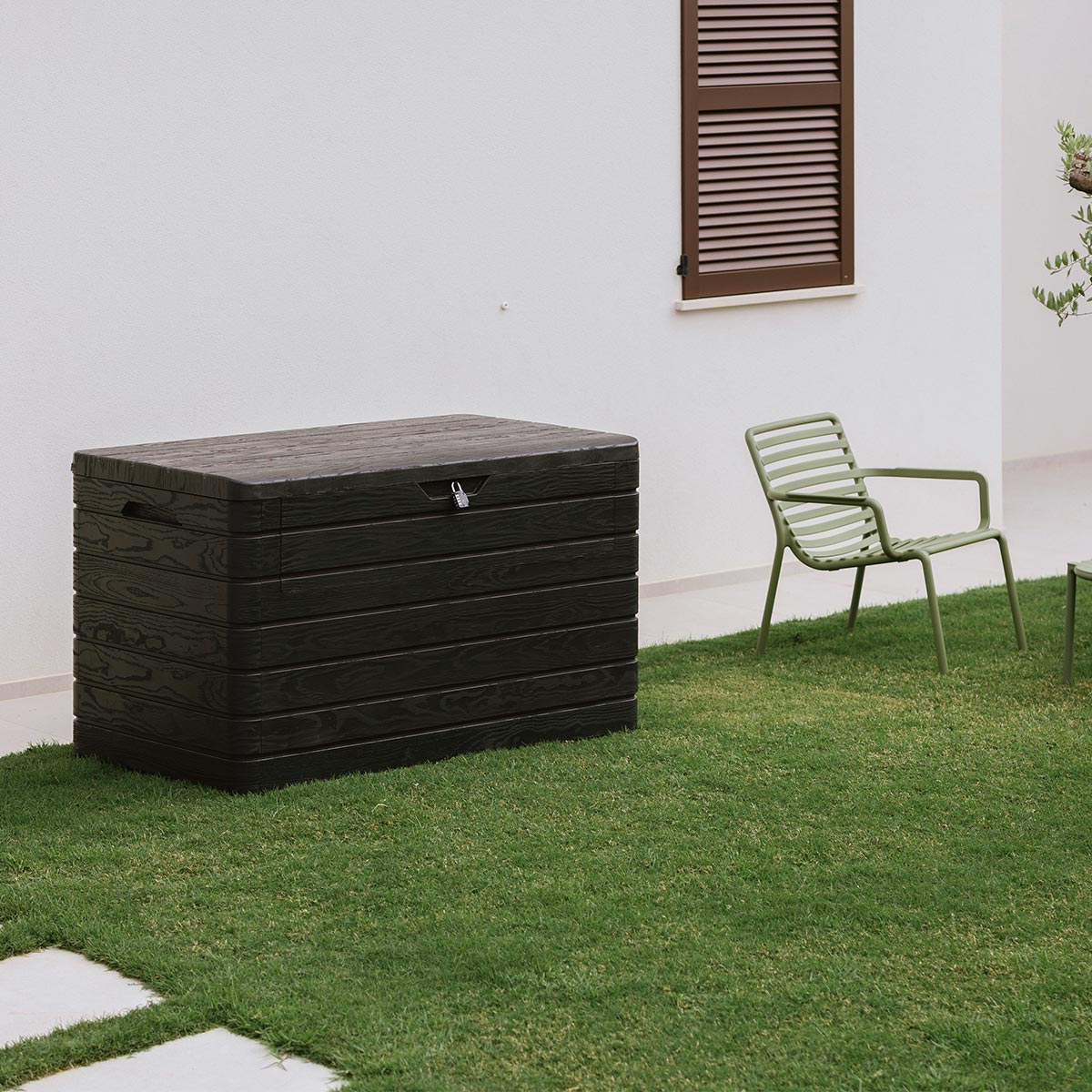 Un coffre de rangement sombre sur une pelouse à côté d'une chaise verte.