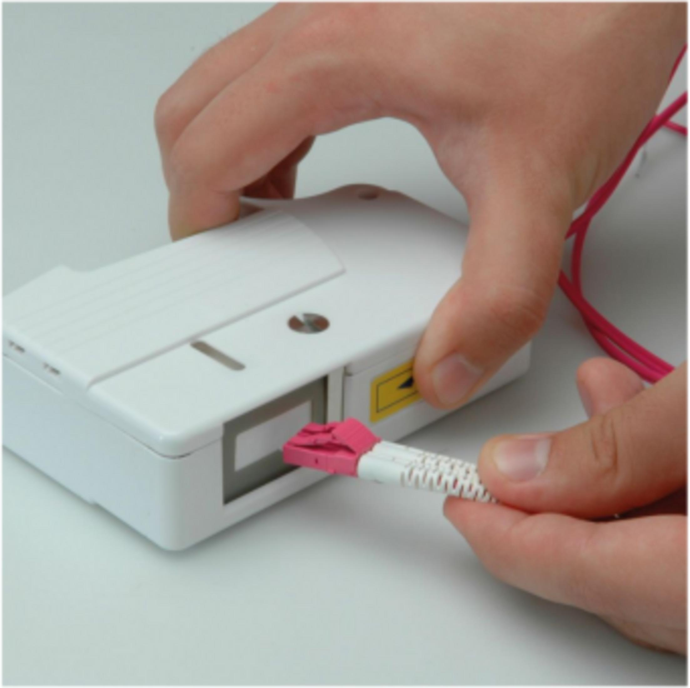 Eine Hand steckt einen rosa Stecker in ein weißes Gerät.