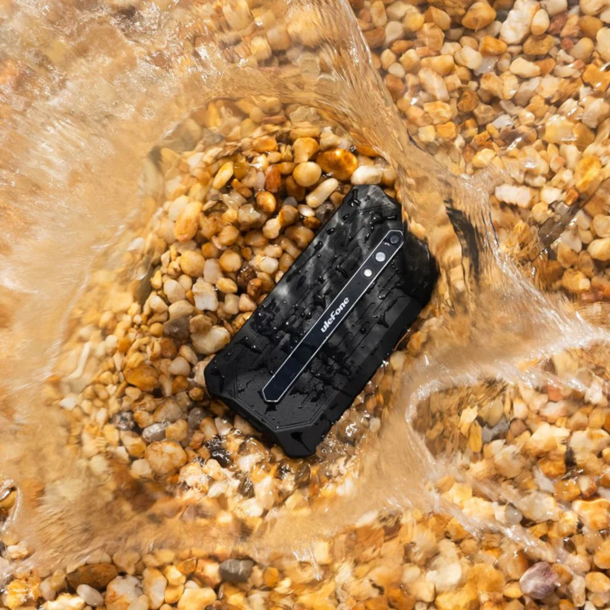 Czarny, wytrzymały telefon Ulefone leży na mokrych, kolorowych kamykach, podczas gdy po nim płynie woda.