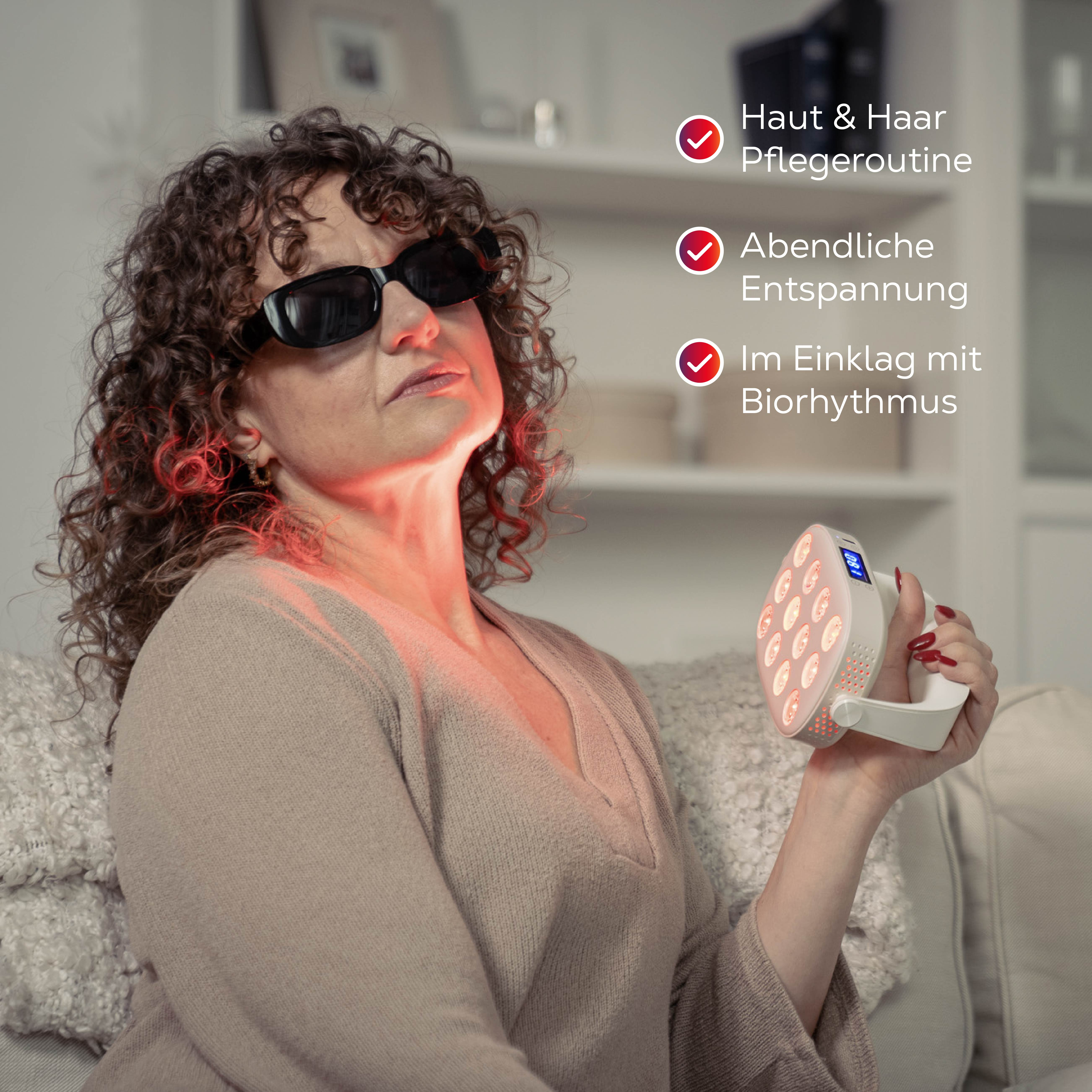 Frau mit Locken, Sonnenbrille und rotem Licht auf dem Hals hält ein Gerät.