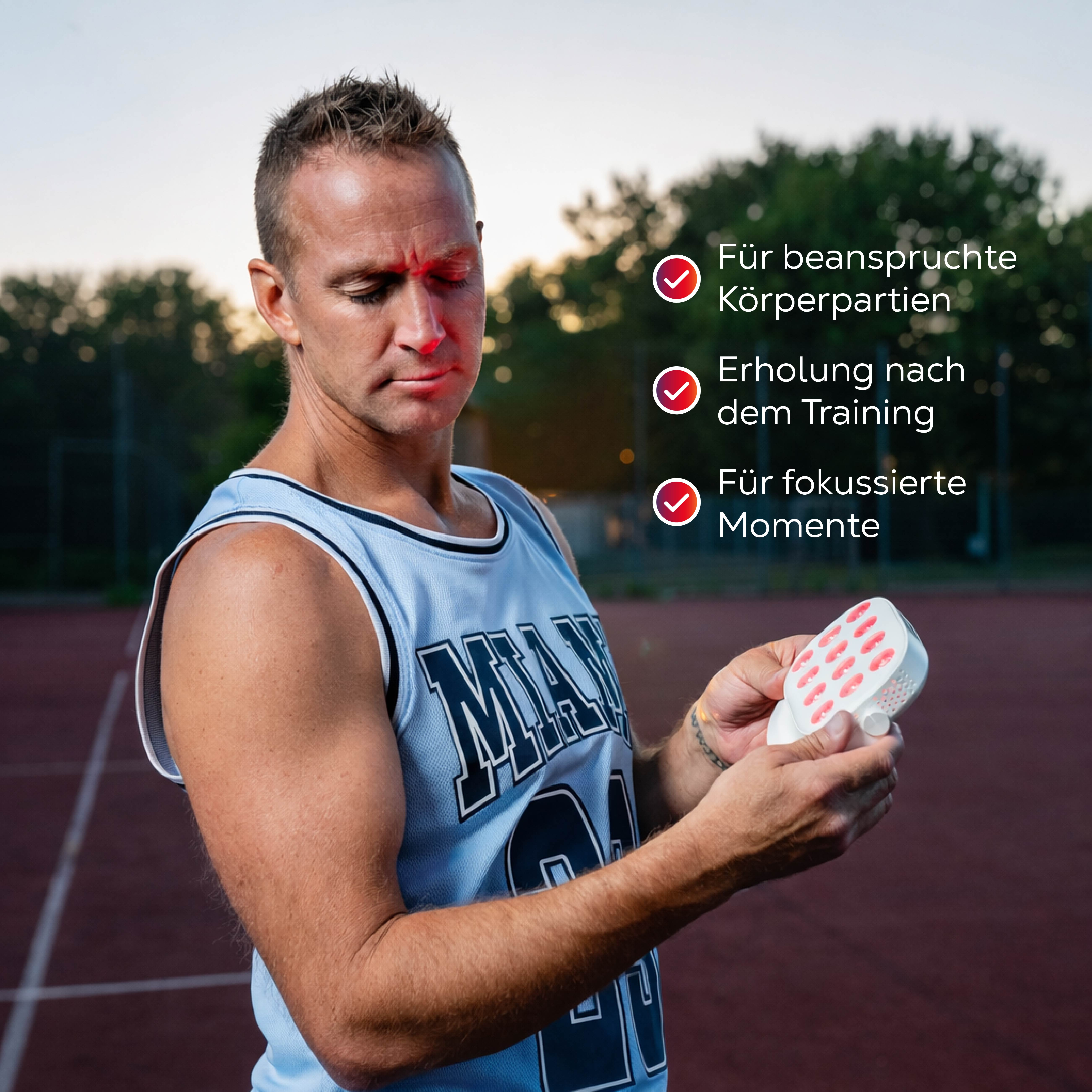 Mann im blauen Basketballtrikot hält Rotlichtgerät. Rotes Licht im Gesicht.