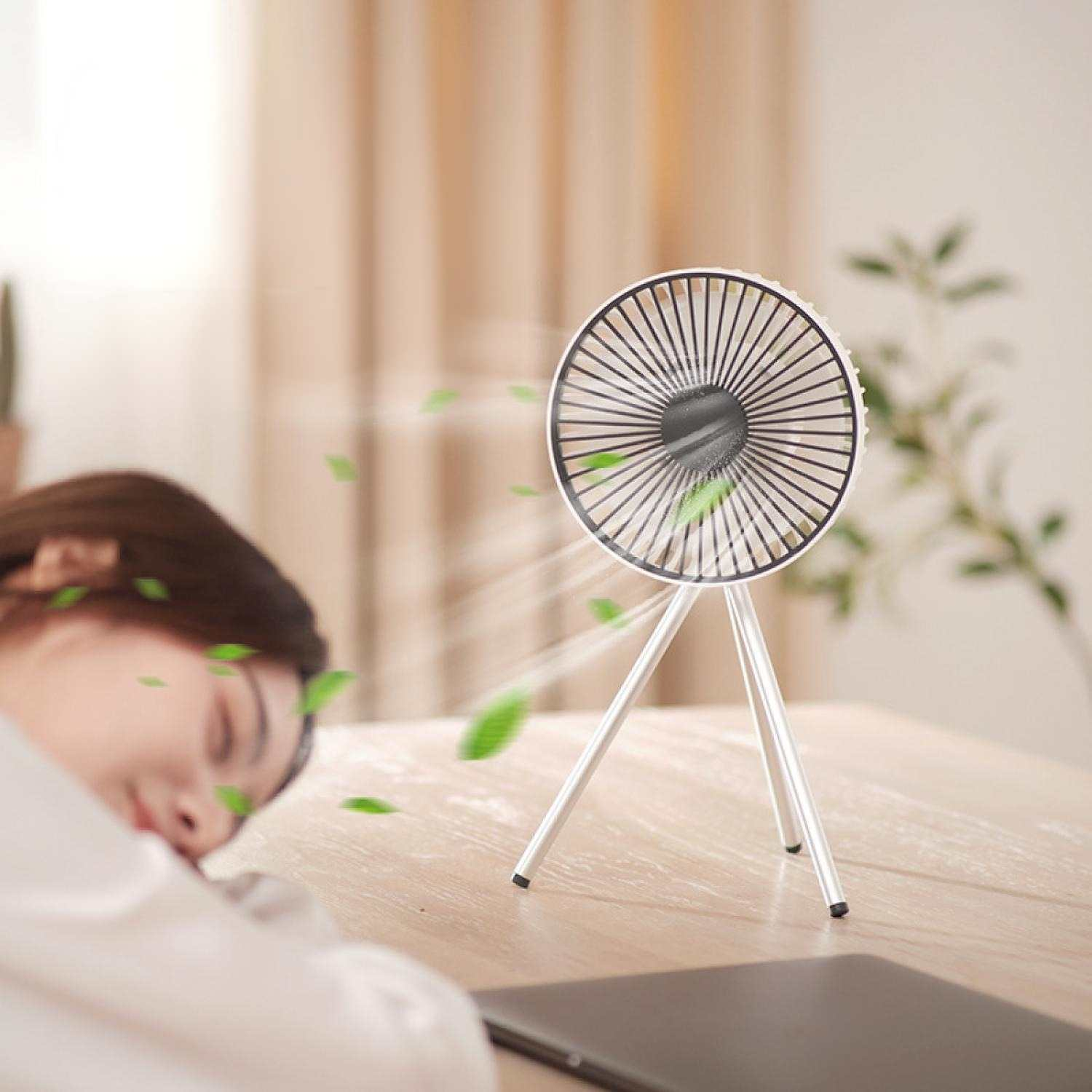 Ein kleiner Ventilator auf einem Stativ bläst grüne Blätter auf eine schlafende Person.