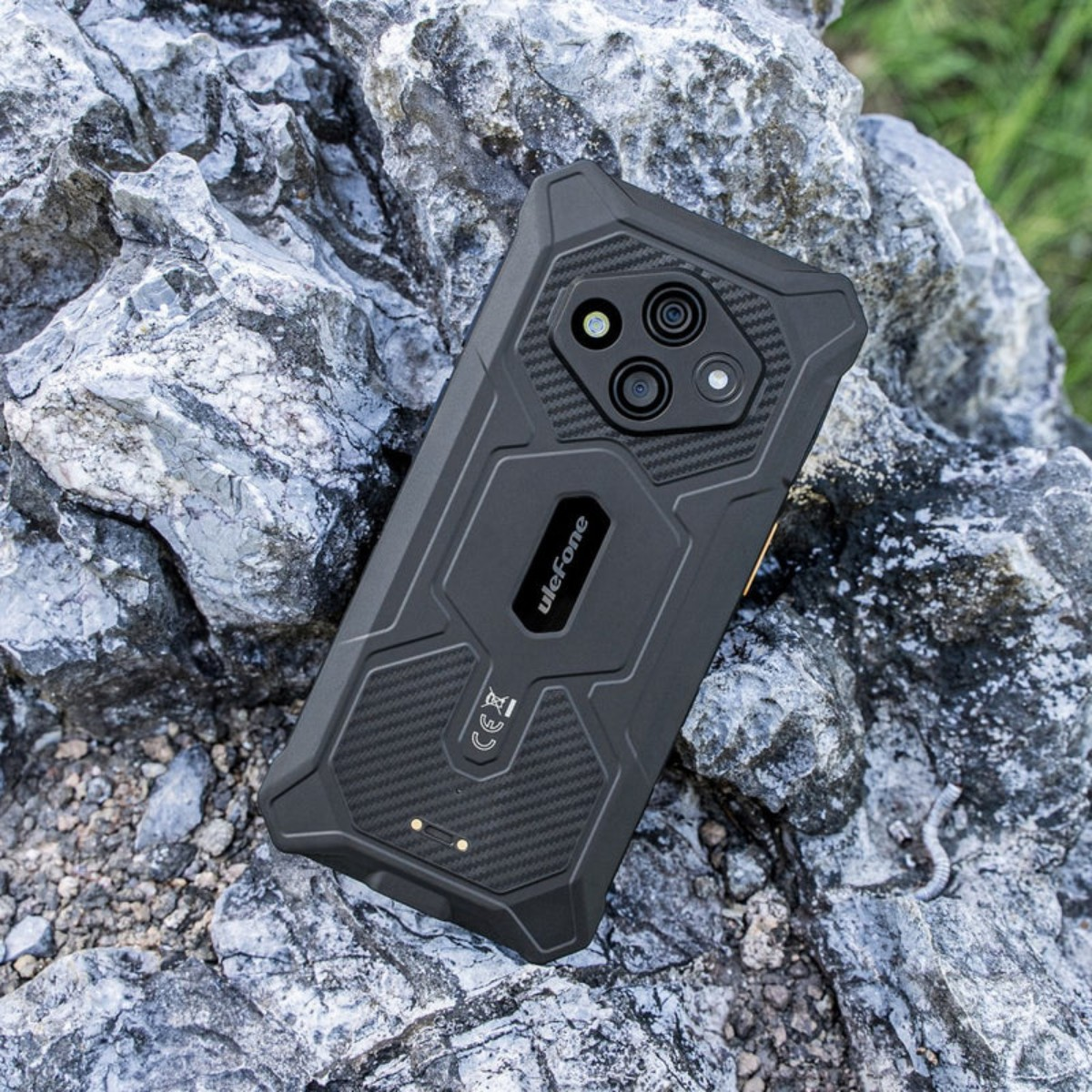 Czarny telefon Ulefone leży na szorstkich skałach, z zieloną roślinnością w tle.