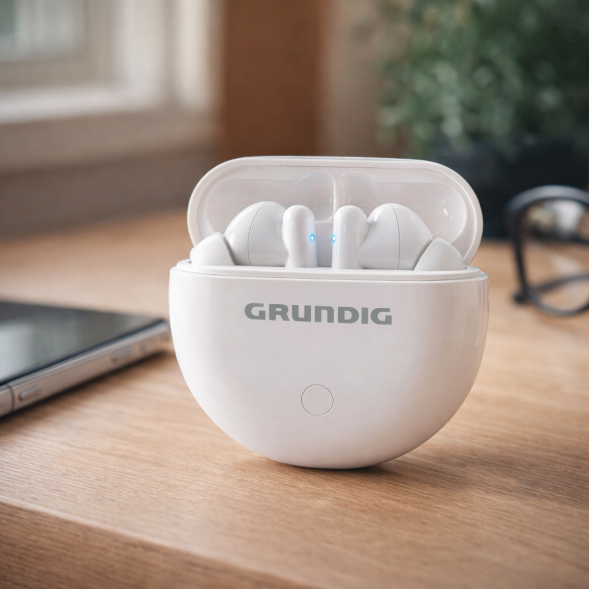 Weiße Grundig kabellose Ohrhörer im offenen Etui auf einem Holztisch mit Handy und Brille.