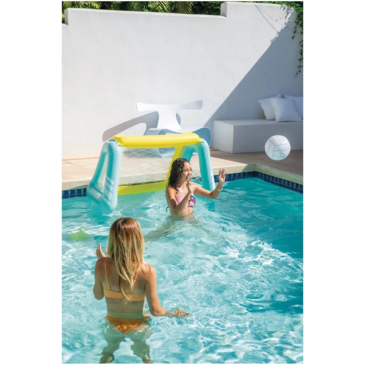 Zwei Mädchen spielen mit einem aufblasbaren Tor und Ball in einem Pool.