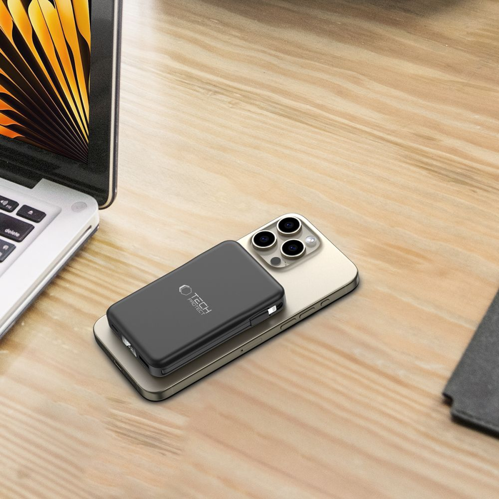 Ein graues Powerbank liegt auf einem goldenen Smartphone neben einem Laptop.