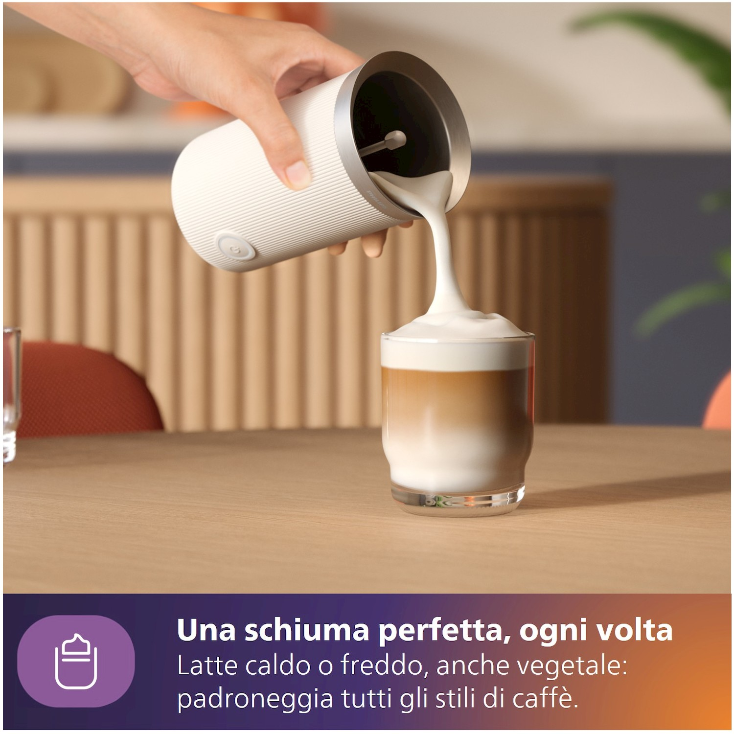 Ein Milchaufschäumer gibt cremigen Schaum in ein Glas mit Kaffee und Milch.