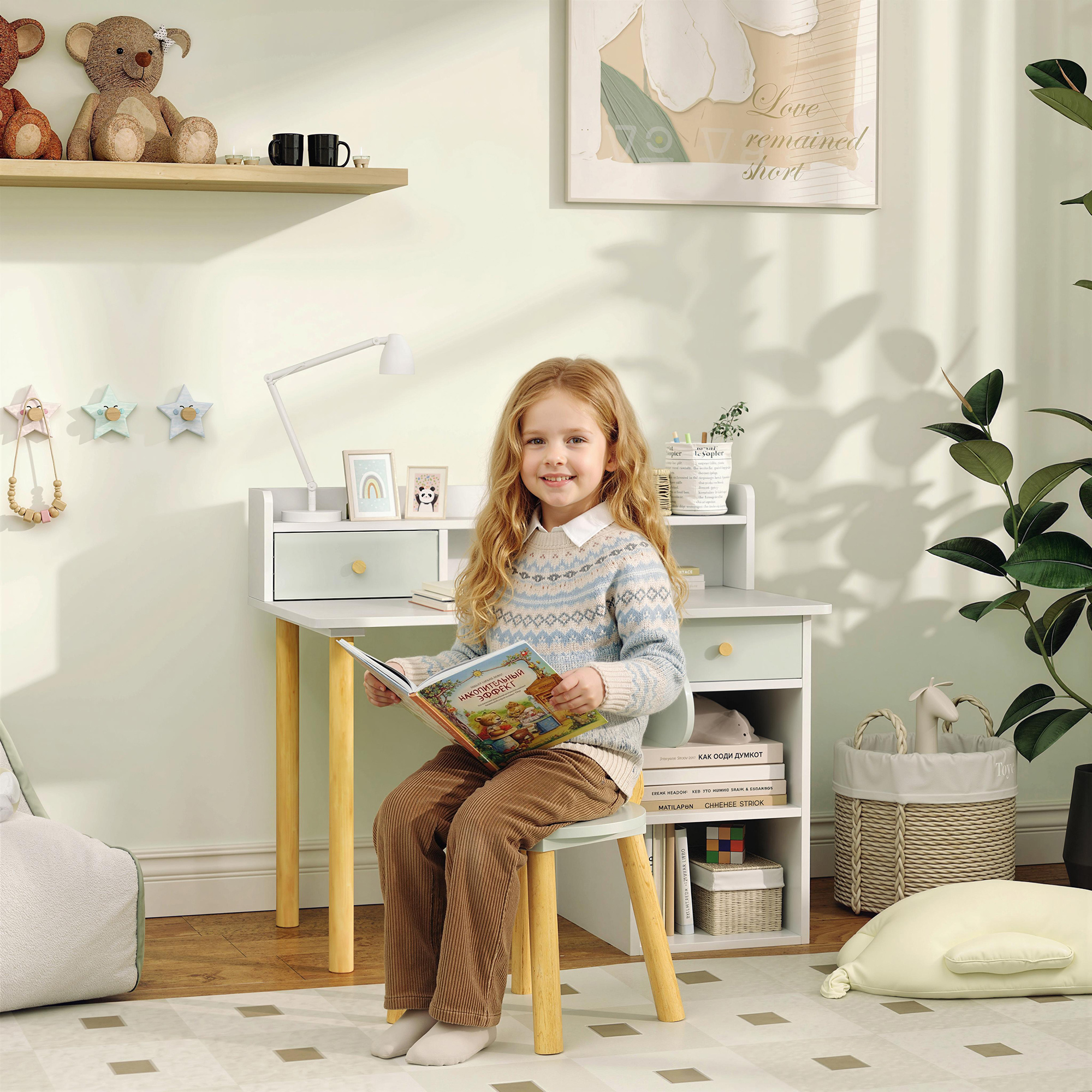 Una niña rubia se sienta en un escritorio leyendo un libro. Lleva un suéter estampado.