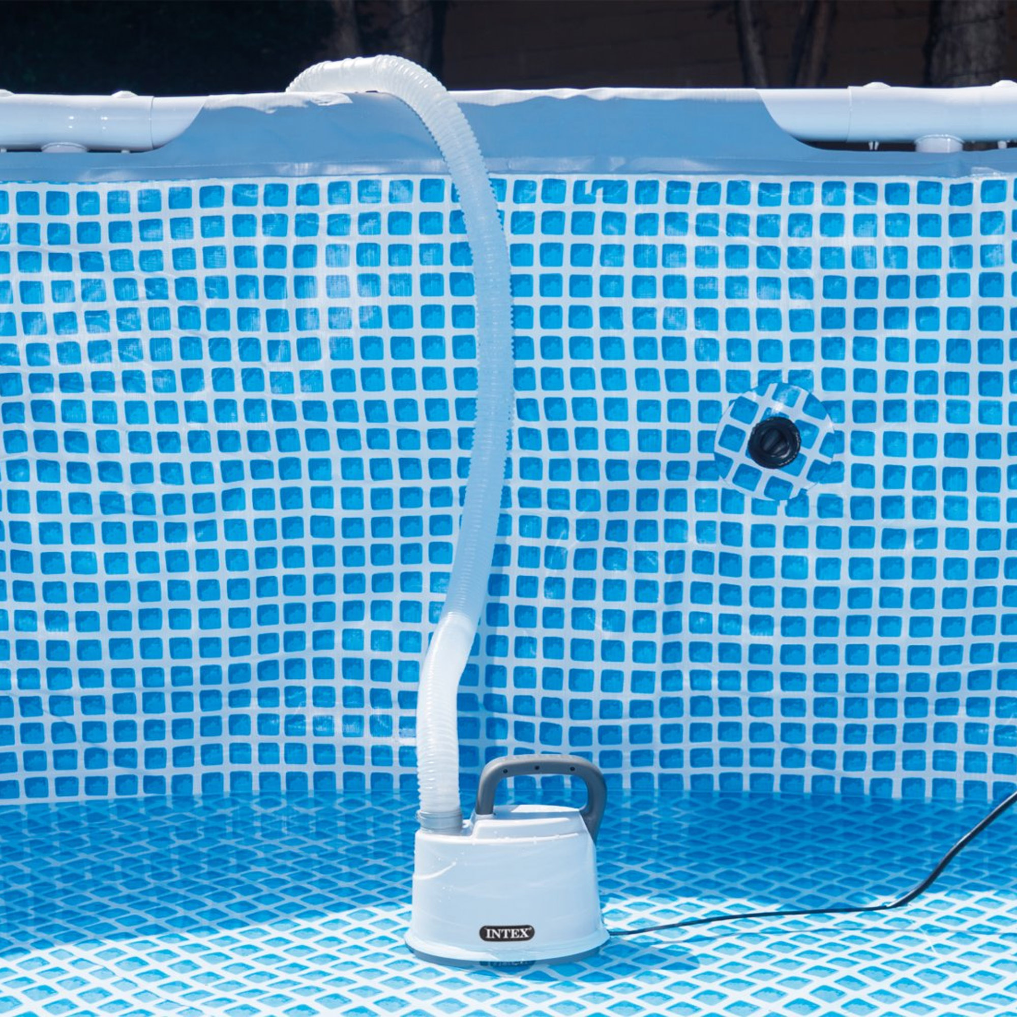 Un limpiador de piscina blanco con manguera está en una piscina vacía con patrón de cuadros azules.