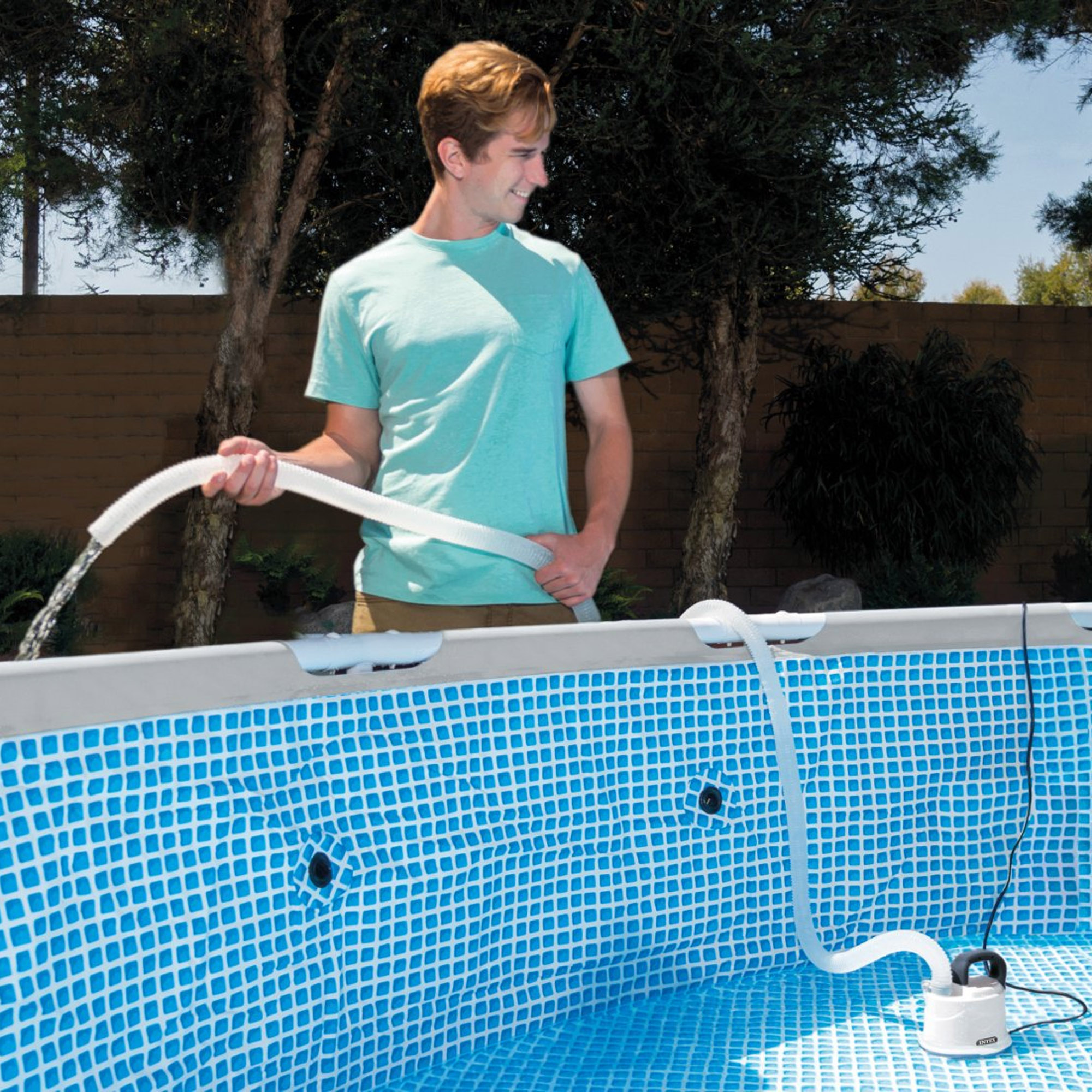 Hombre con camisa azul agrega agua a la piscina con manguera. Bomba de filtro visible.