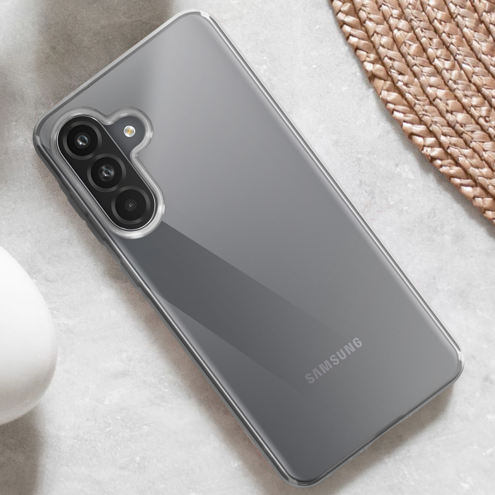 Una cover trasparente per telefono con tripla fotocamera e logo Samsung su superficie testurizzata.