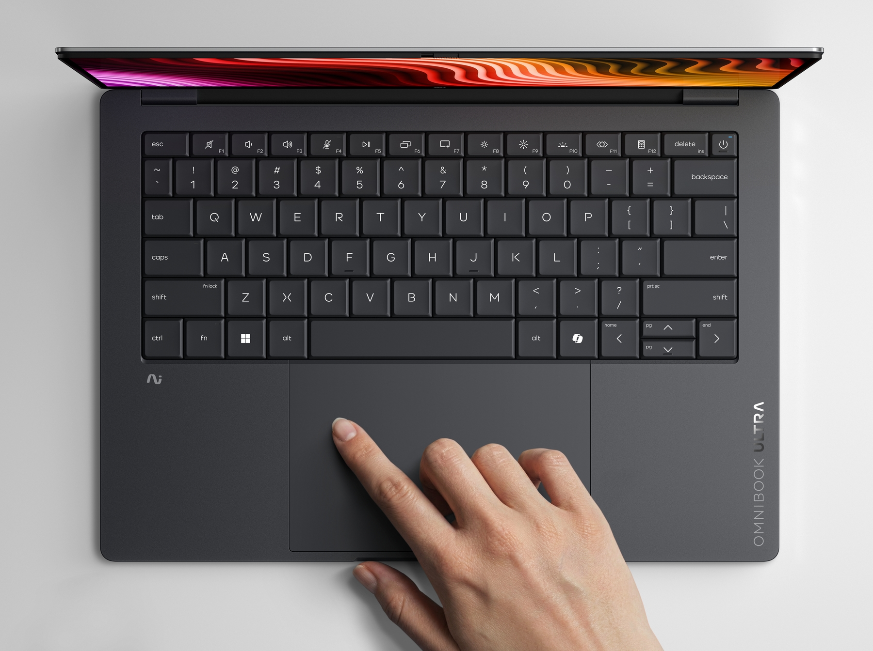 Una mano usa il touchpad di un laptop scuro con schermo illuminato.