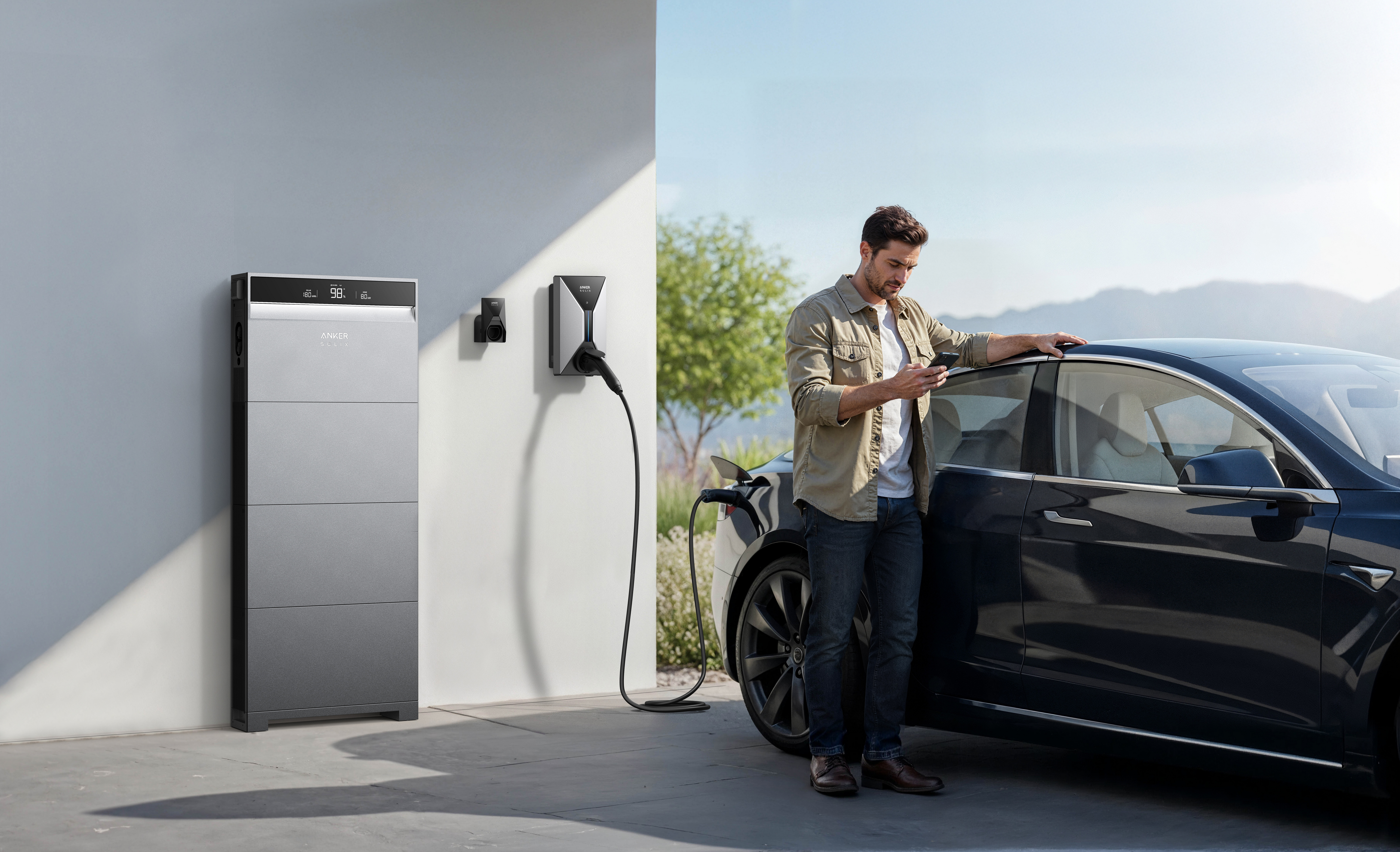 Ein Mann prüft sein Handy neben einem Elektroauto, das an eine Wandladestation angeschlossen ist.