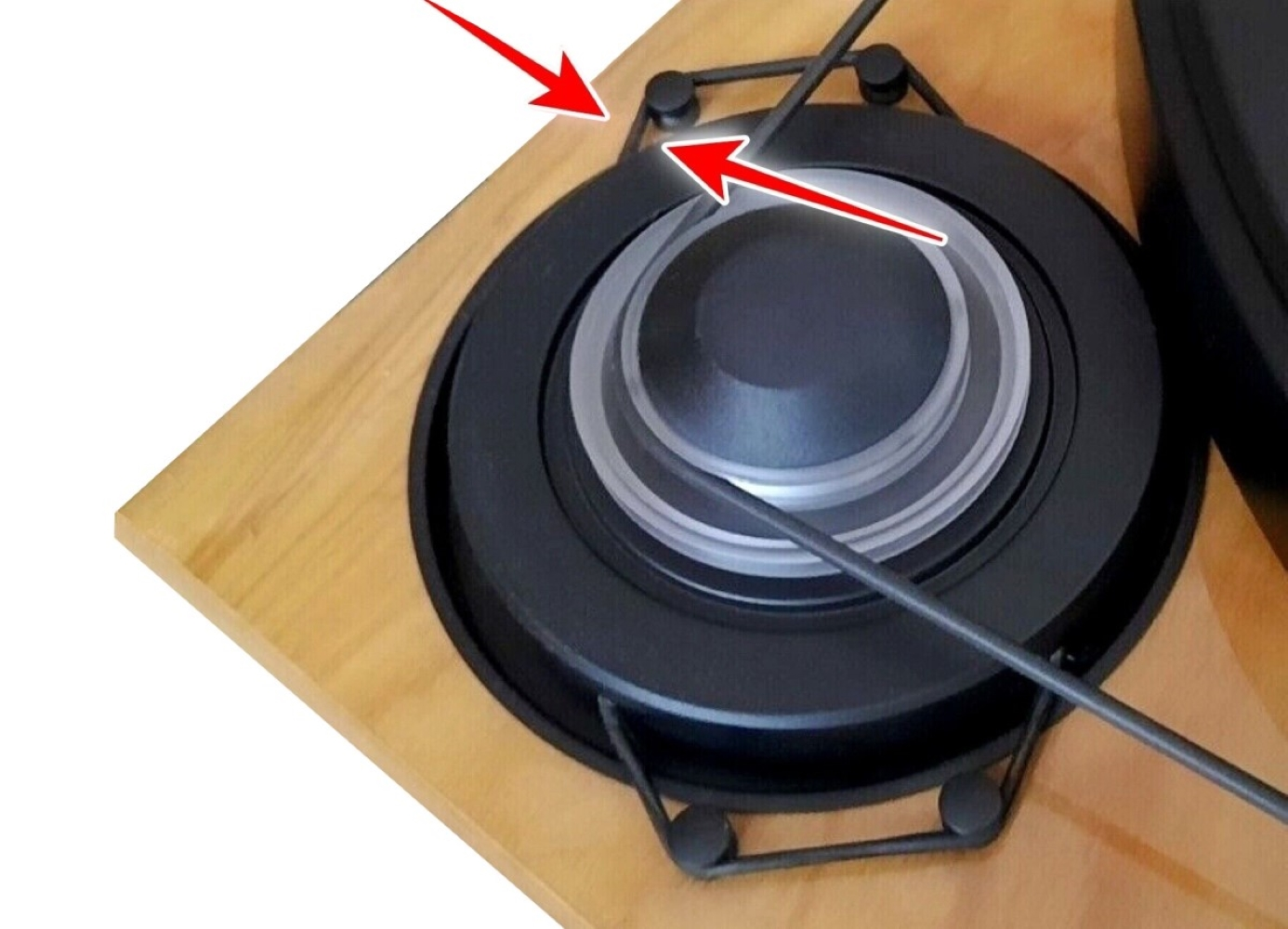 Kratka głośnika na drewnianej obudowie, zaznaczona czerwonymi strzałkami.