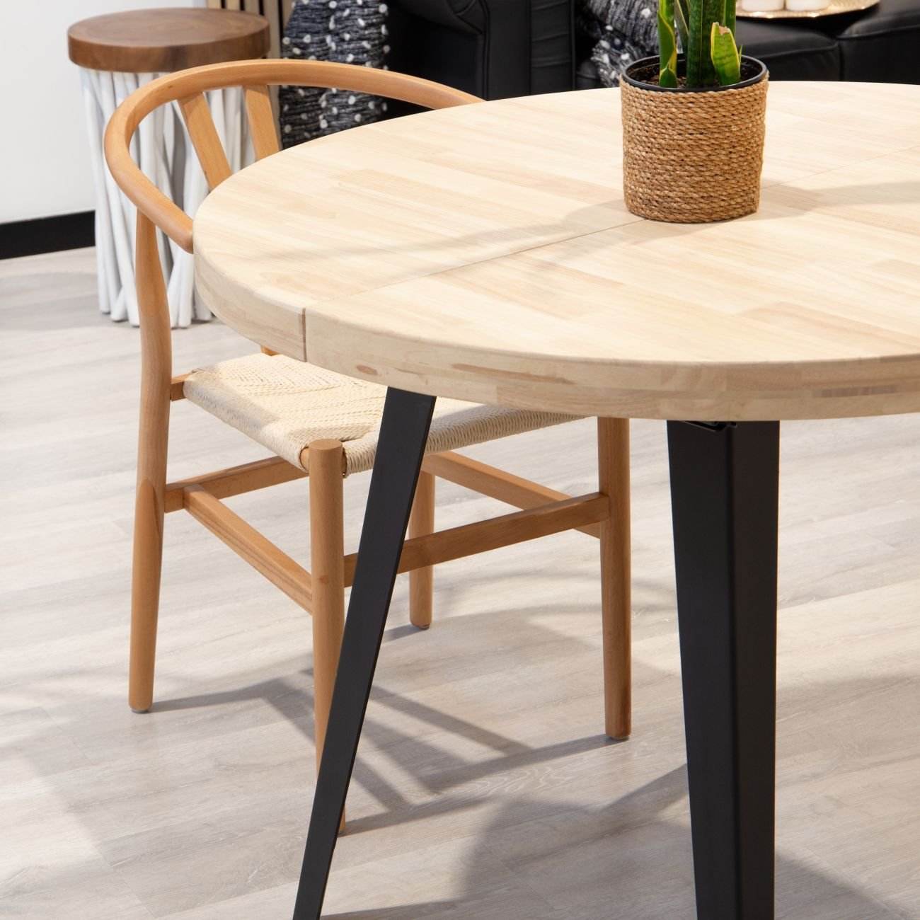Mesa redonda de madera con patas de metal negro y una planta en maceta.