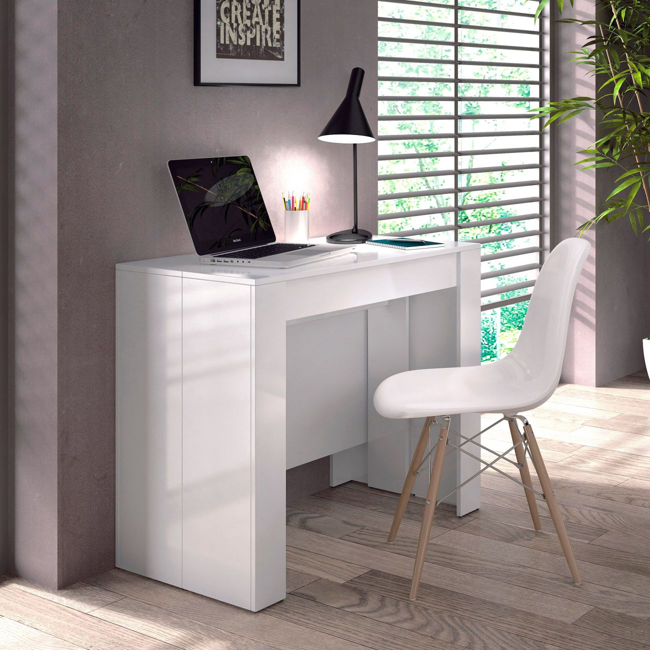 Un escritorio blanco con portátil, lámpara y bolígrafos, junto a una silla. Una ventana al fondo.