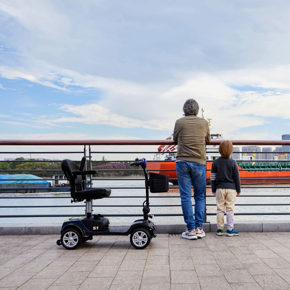 Un hombre y un niño están junto a un río, al lado de un scooter, mirando un barco.