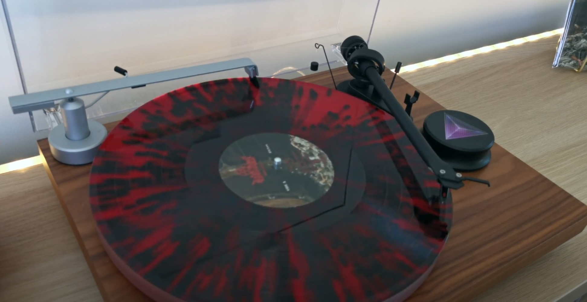 Gramofon z czerwono-czarną płytą, ramieniem i drewnianą podstawą.