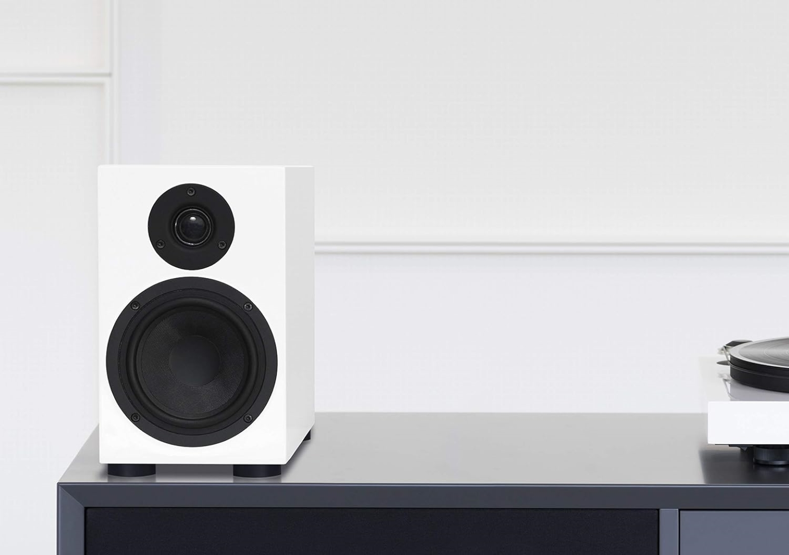 Biały głośnik z czarnym głośnikiem wysokotonowym i niskotonowym stoi na stole.