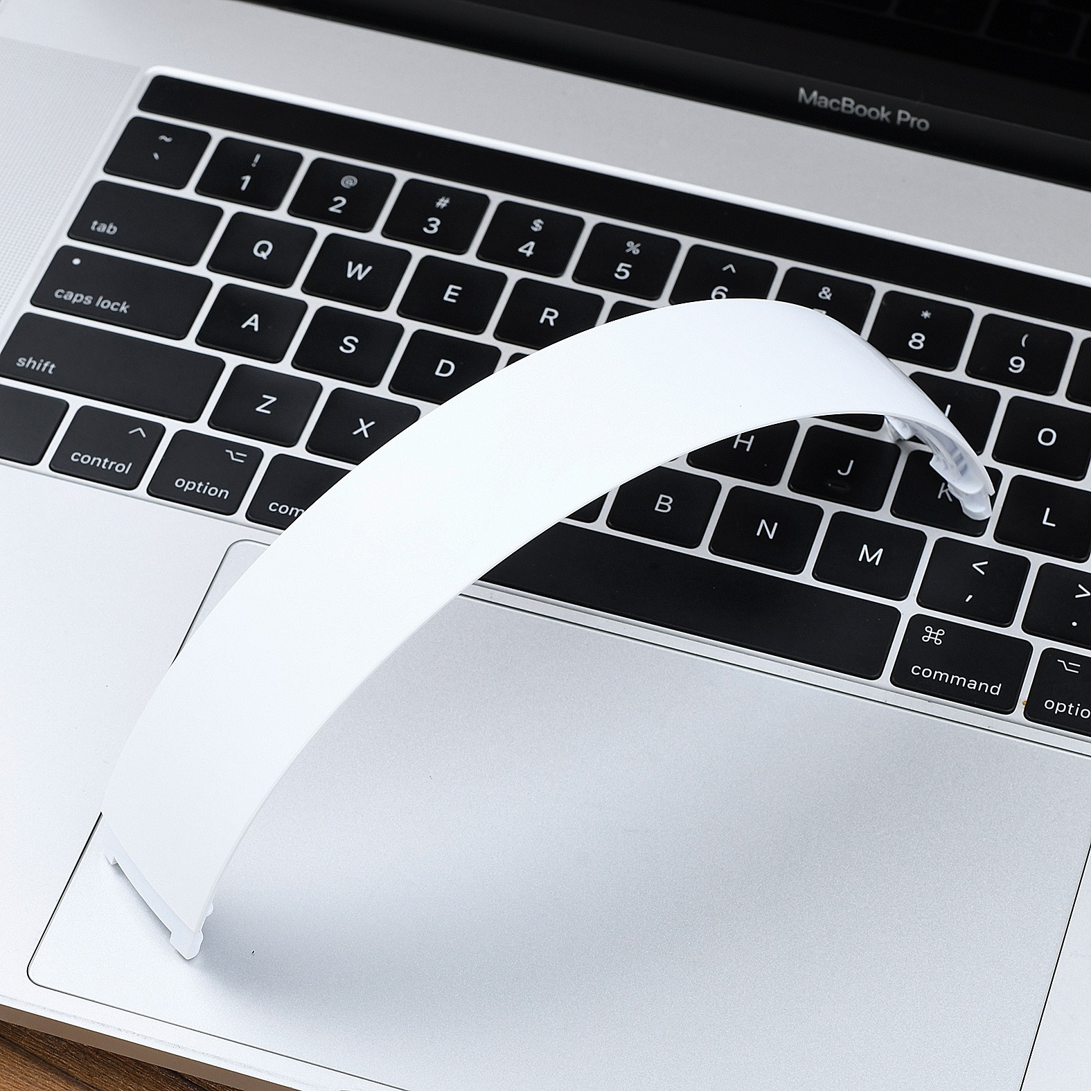 Un oggetto bianco curvo poggia sulla tastiera argentata di un MacBook Pro.