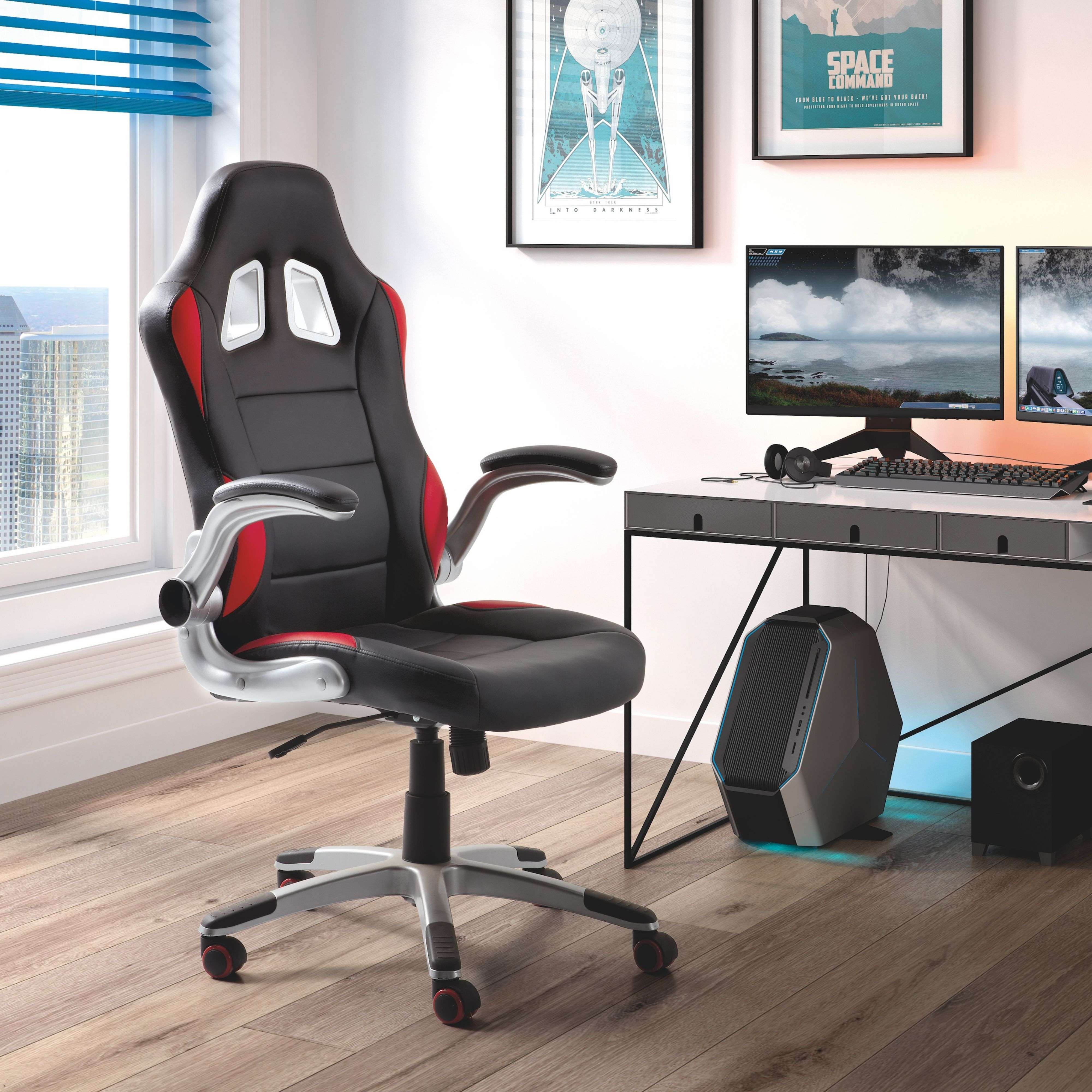 Una silla gamer negra junto a un escritorio con ordenadores y arte.