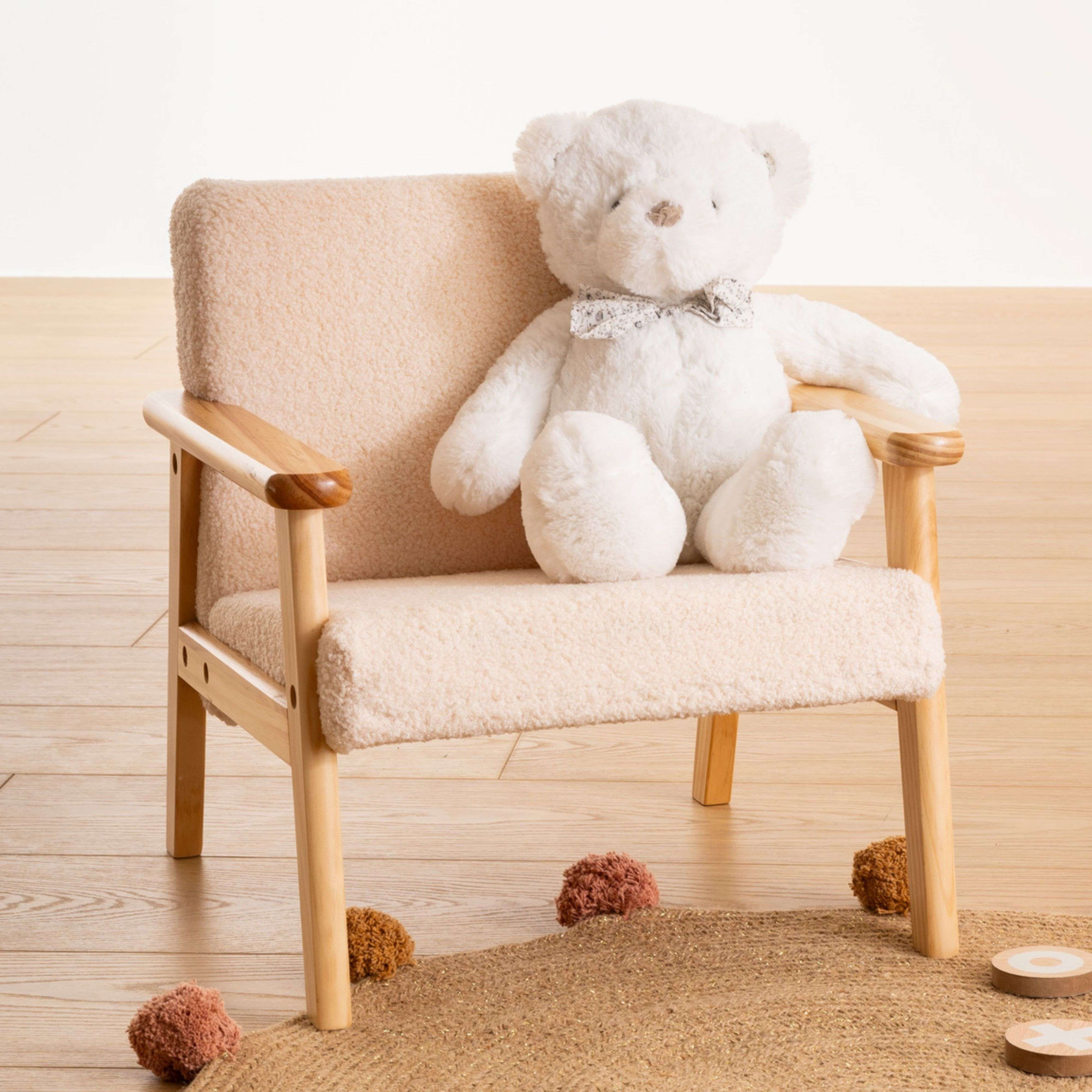 Un oso de peluche blanco se sienta en un sillón beige claro sobre suelo de madera.
