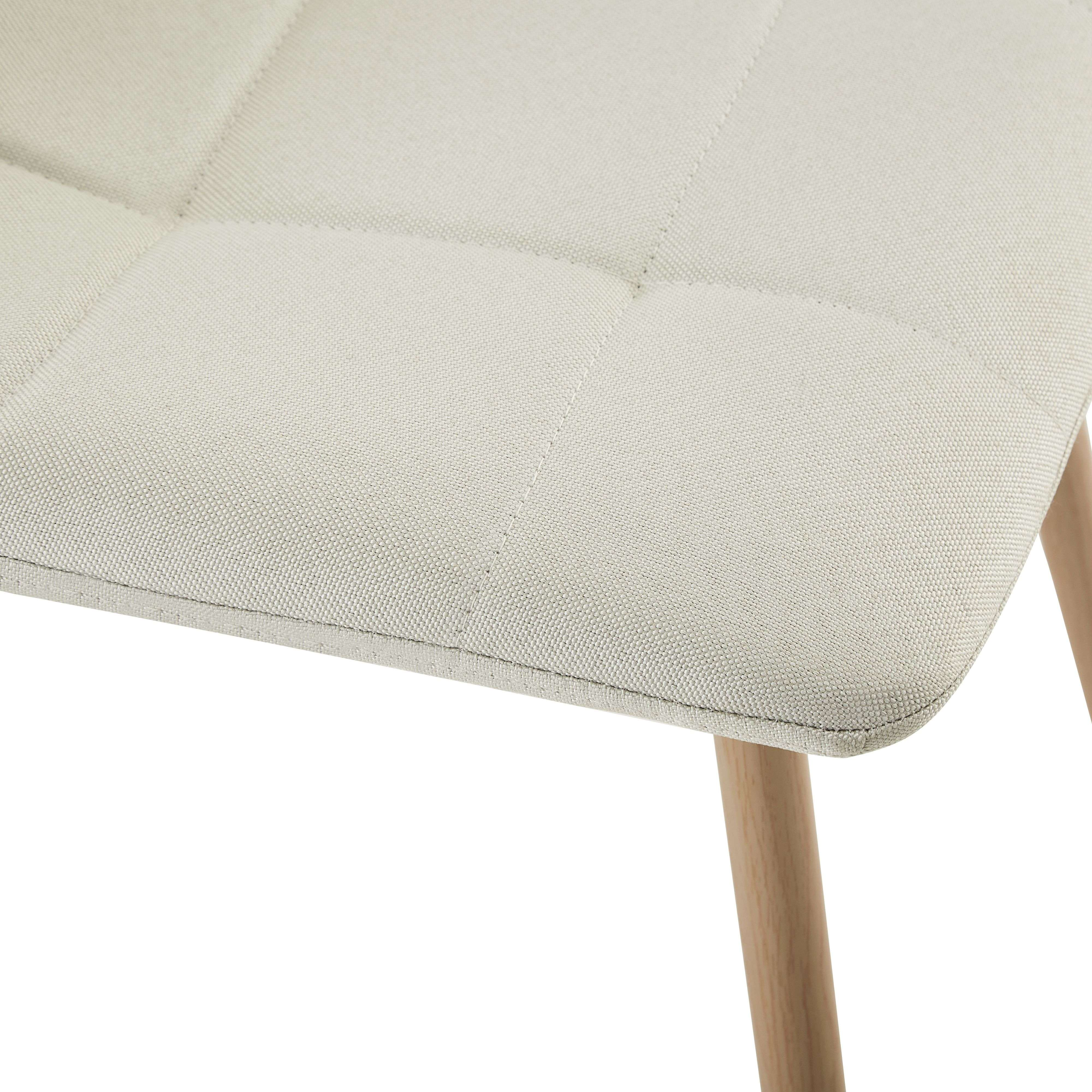 Primer plano de una silla tapizada color crema con patrón de diamantes cosido y patas de madera clara.