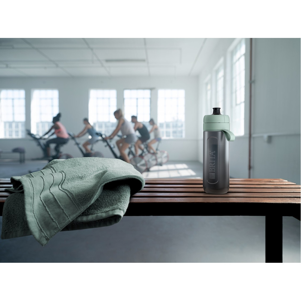 Una borraccia Brita su una panchina di legno in una palestra, con persone che fanno cyclette sullo sfondo.
