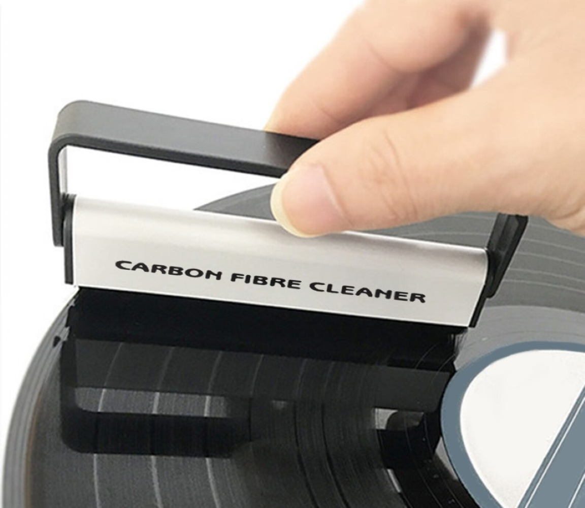 Una mano tiene un pulitore per dischi in fibra di carbonio su un disco in vinile nero.