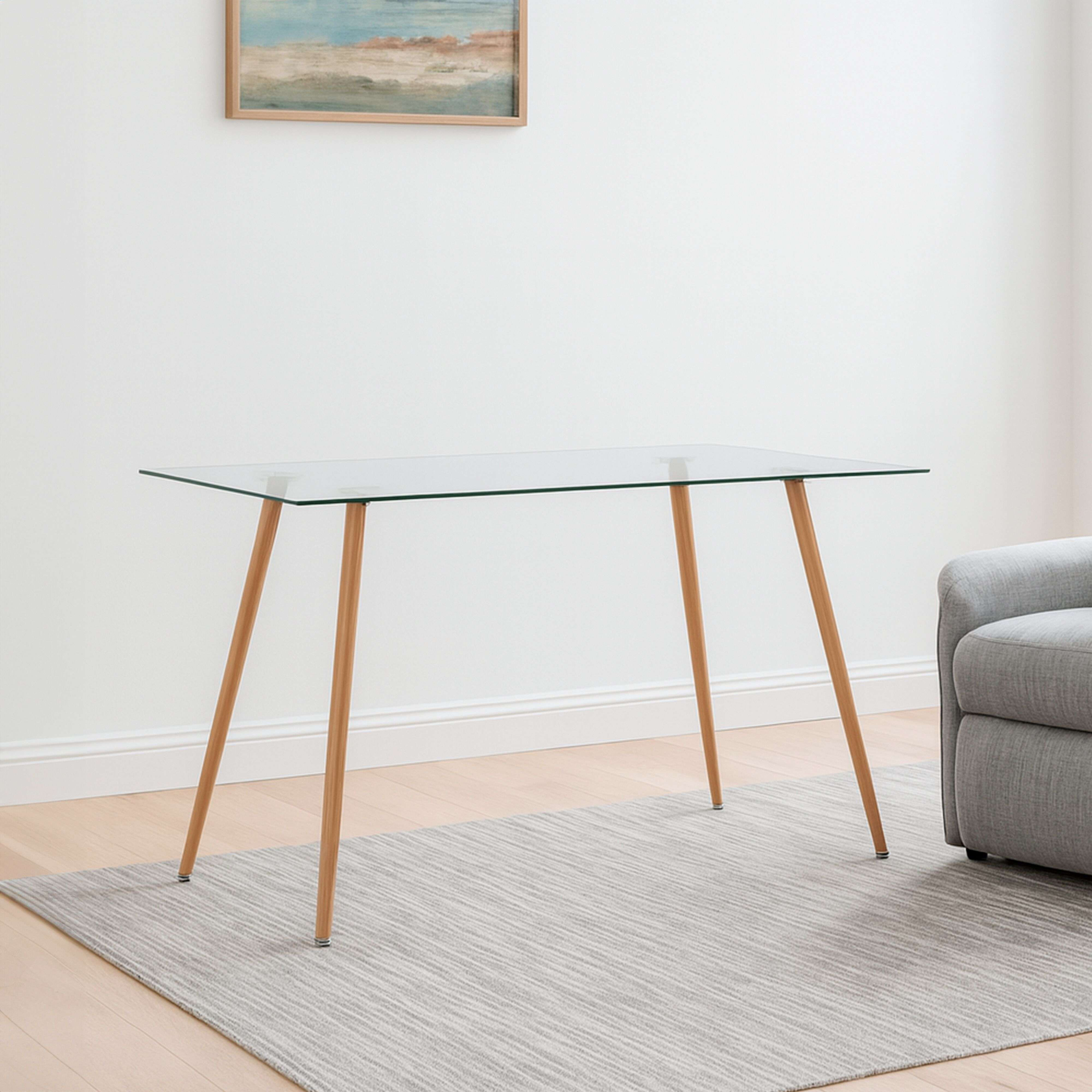 Una mesa de cristal con patas de madera está sobre una alfombra junto a un sofá gris.