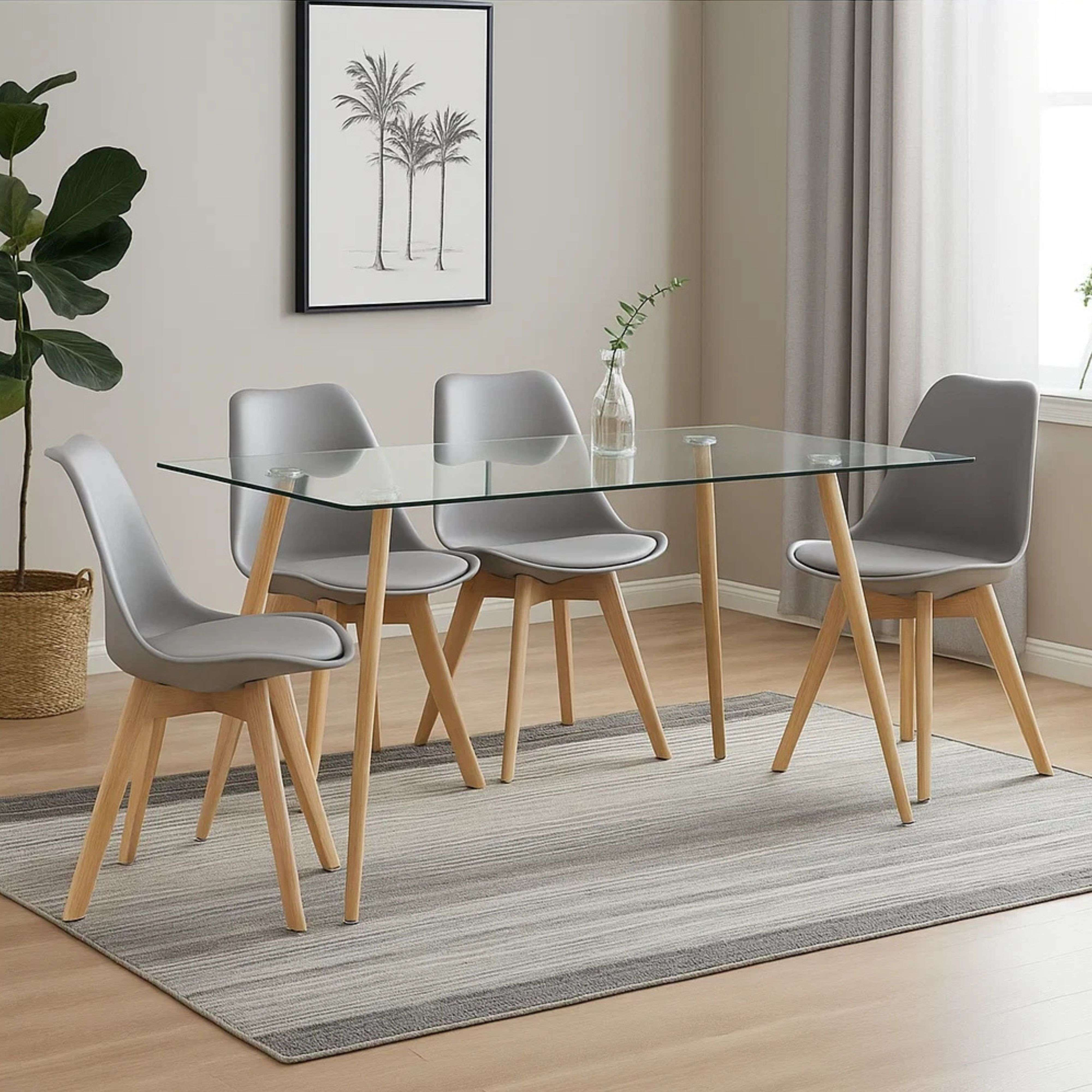 Una mesa de comedor con tapa de cristal y cuatro sillas grises con patas de madera sobre una alfombra.