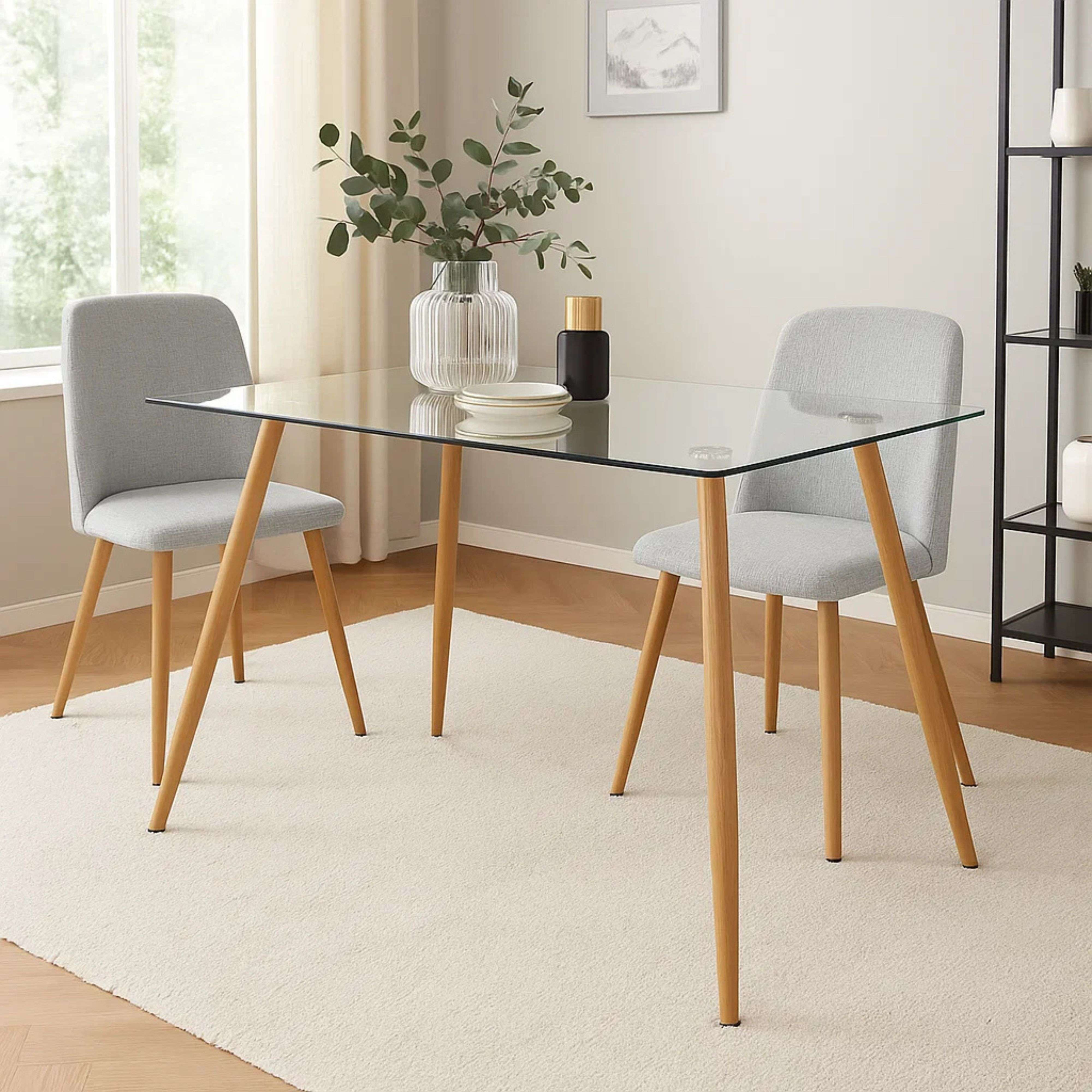 Una mesa de comedor de cristal con patas de madera y dos sillas grises.