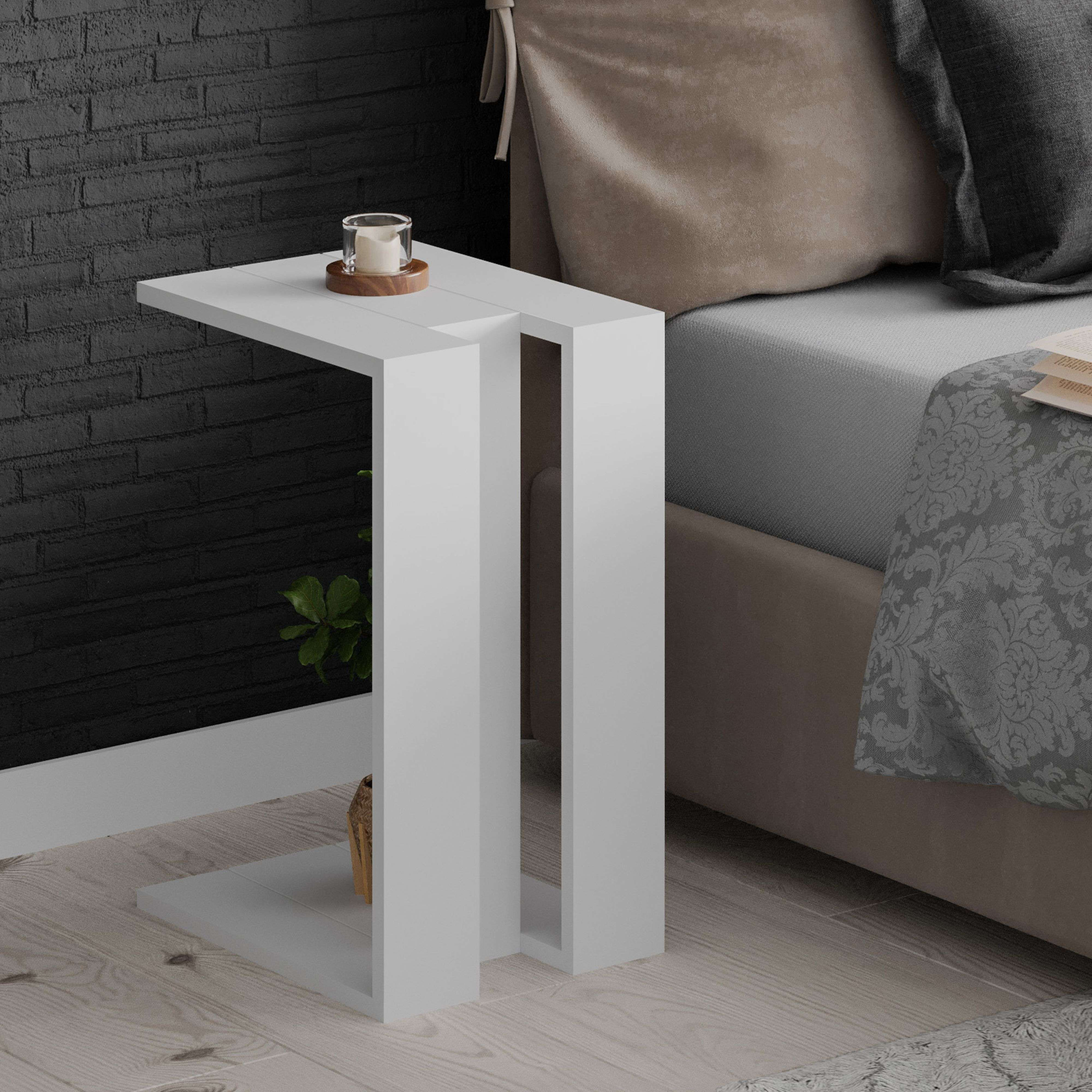 Una mesa auxiliar blanca con vela y planta junto a una cama.