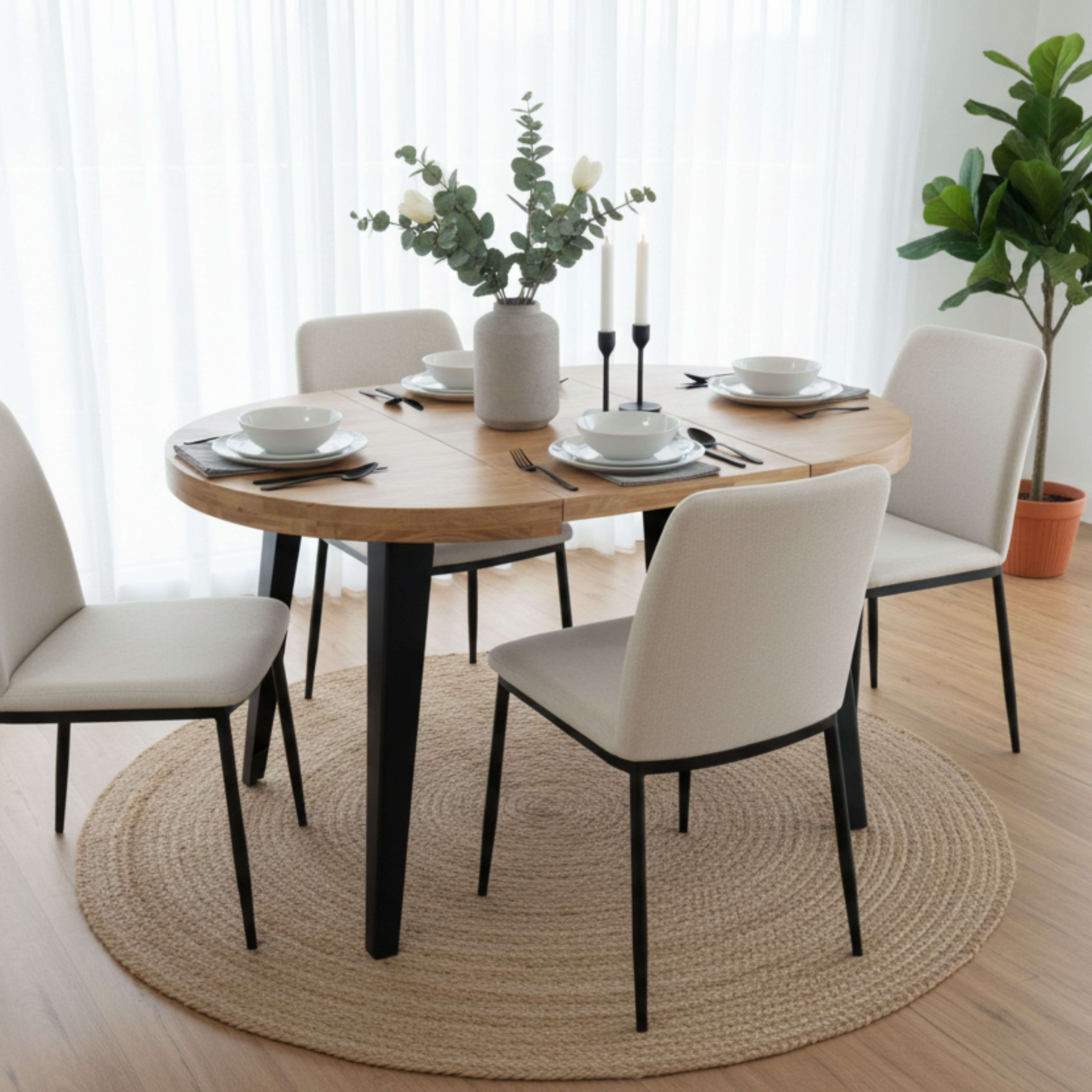 Una mesa ovalada de madera puesta para cenar con cuatro sillas, jarrón y velas.