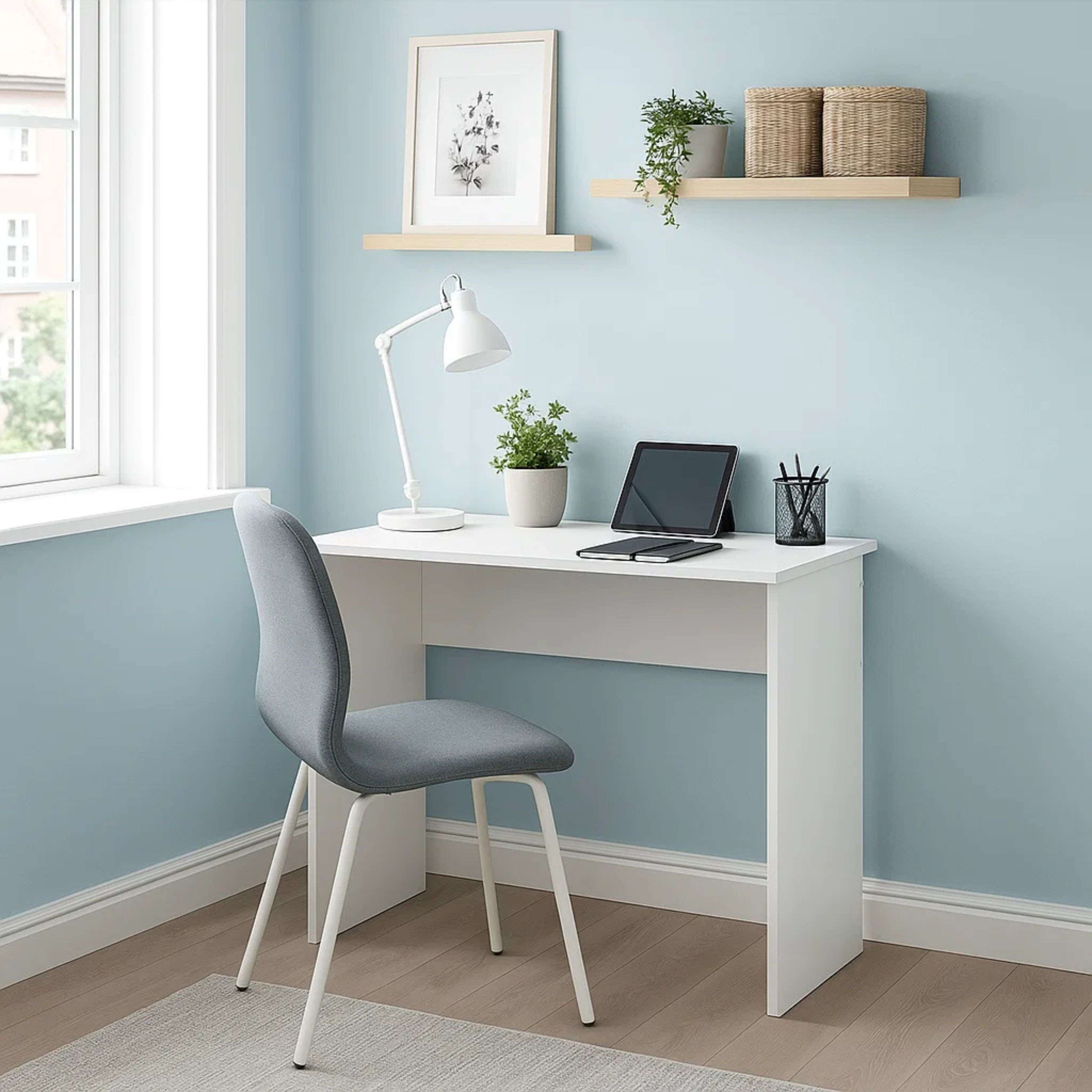 Escritorio blanco con portátil, lámpara y silla frente a pared azul.