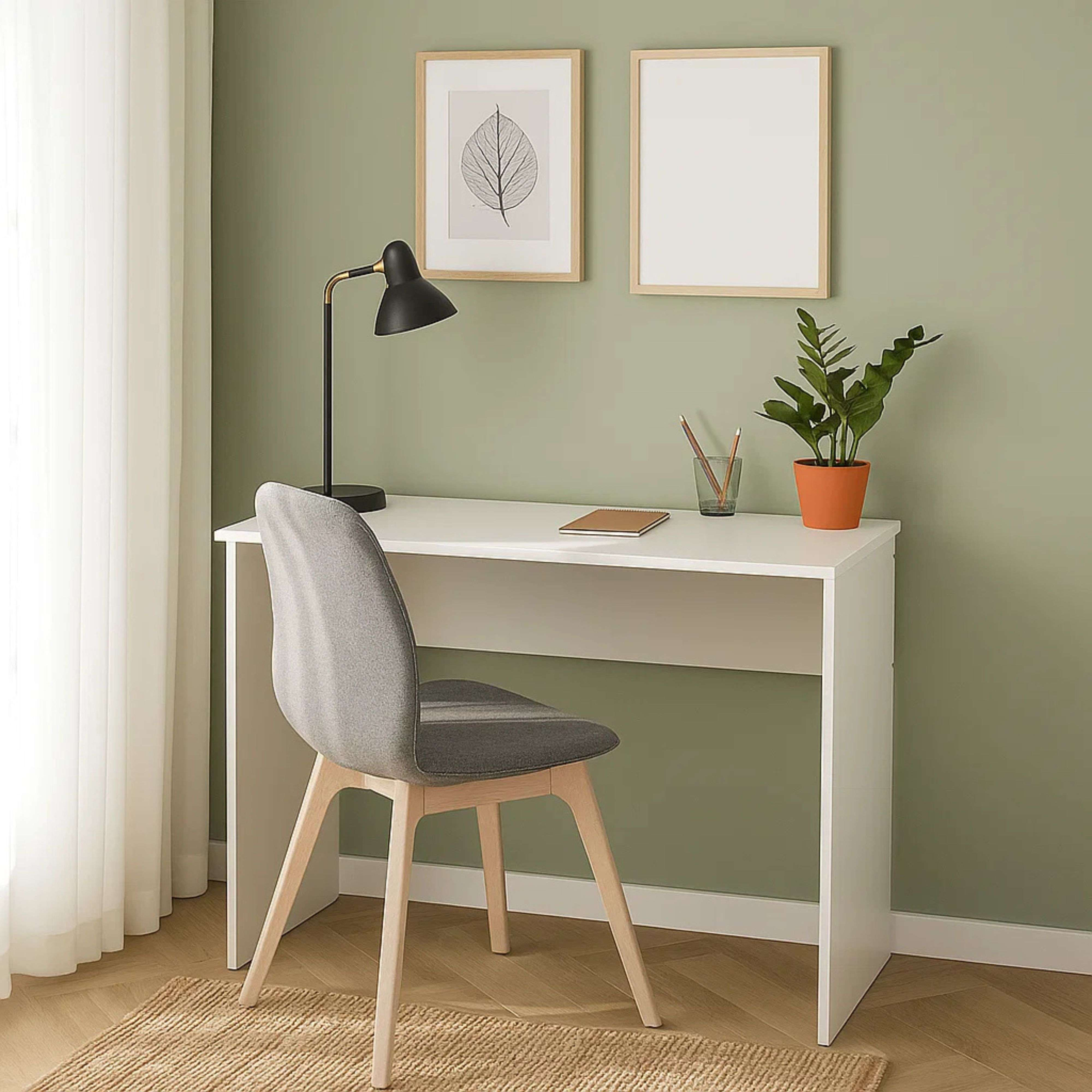 Un escritorio blanco con una silla gris, lámpara y dos cuadros en la pared.