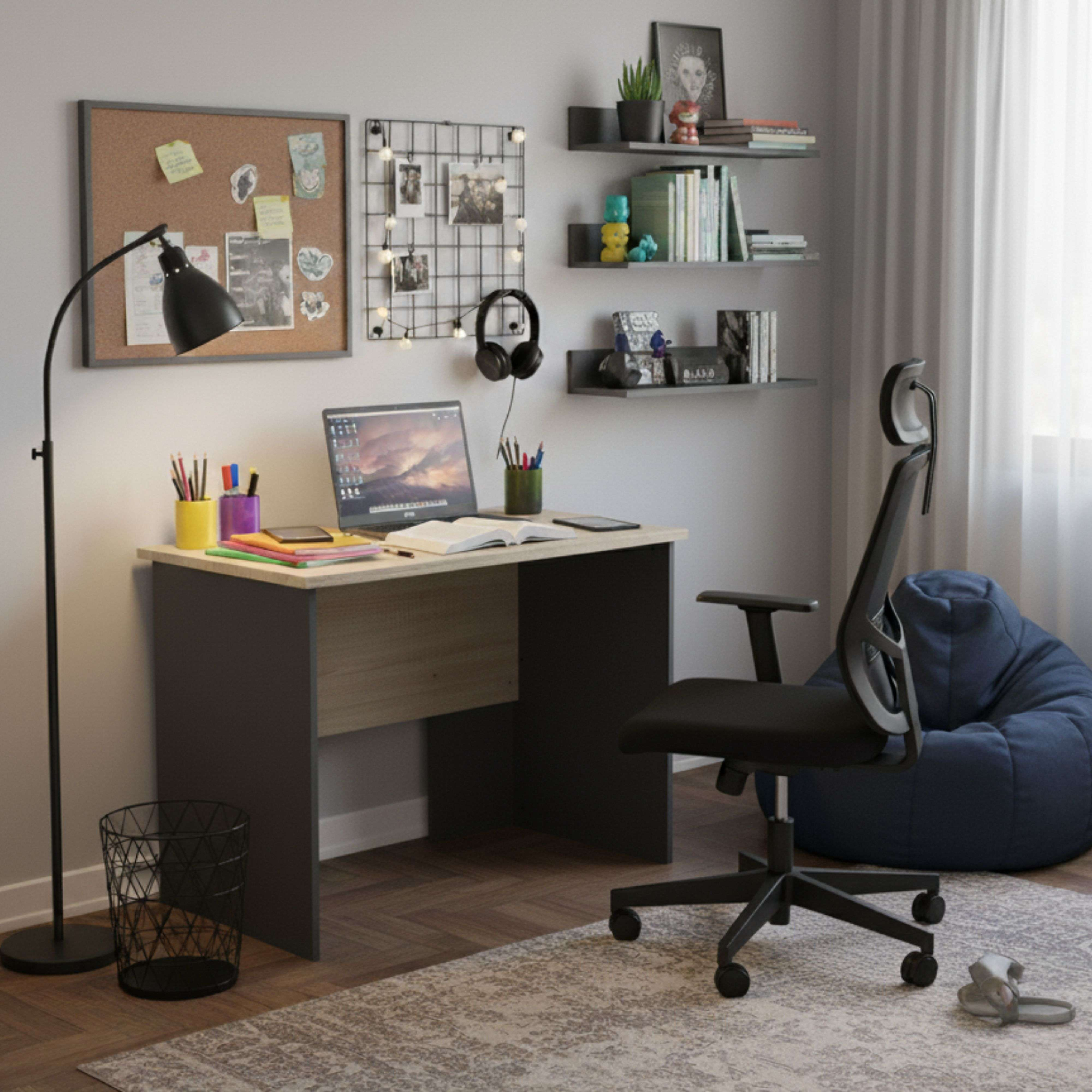 Un escritorio con portátil, libros y material de arte, junto a una silla y un puf.