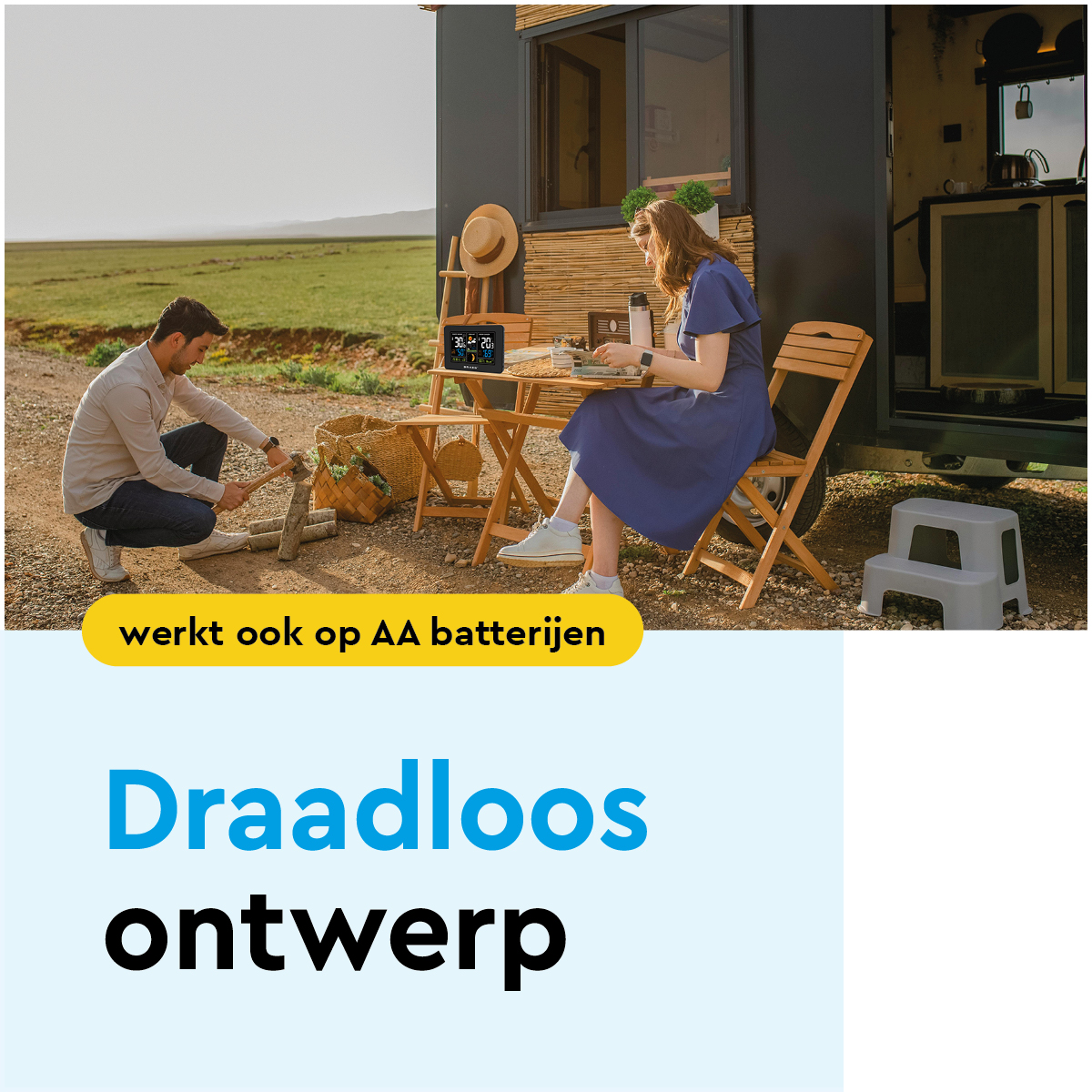 Man hakt hout, vrouw zit aan tafel bij camper. Weerstation op tafel.