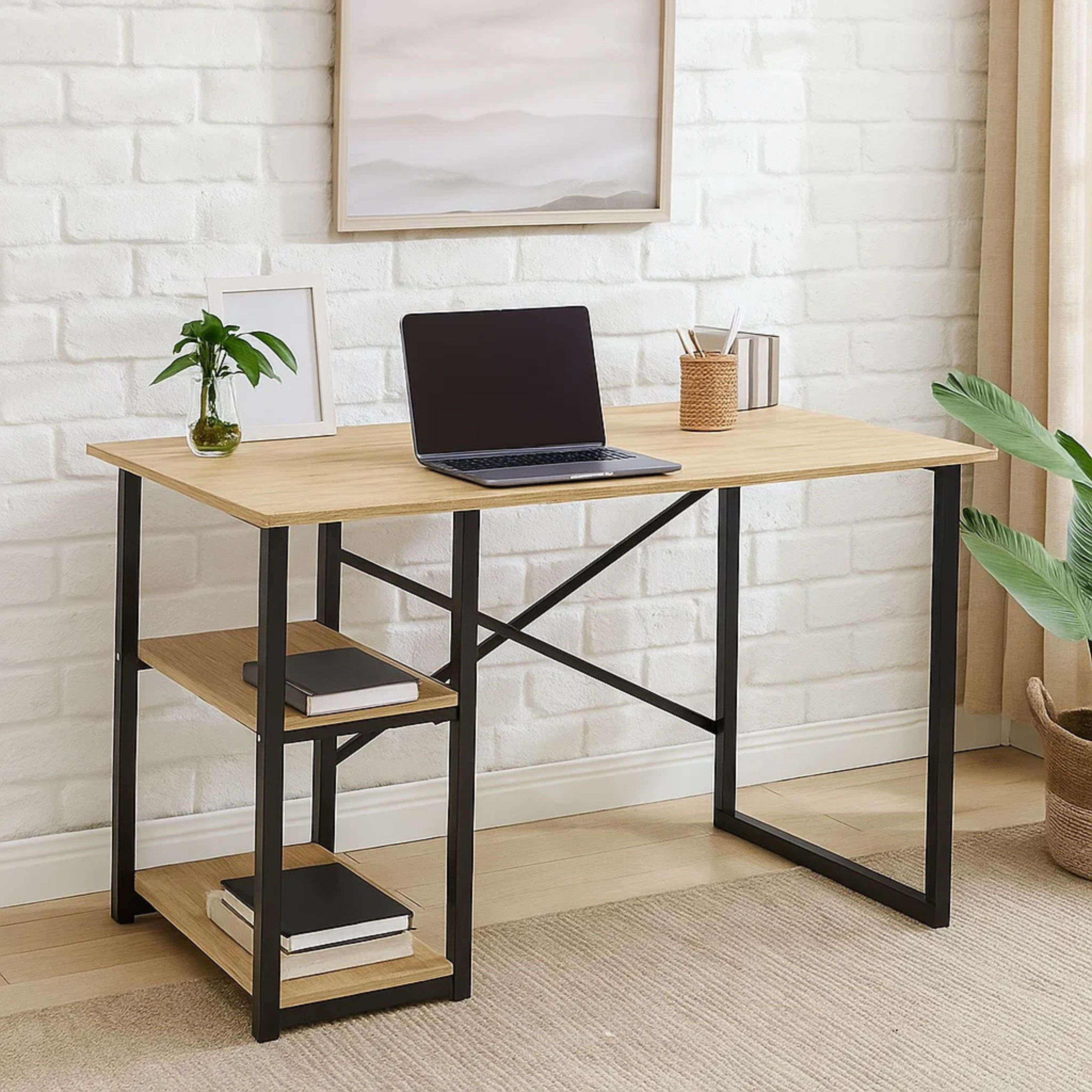 Escritorio con portátil, planta y libros frente a pared de ladrillos blancos.