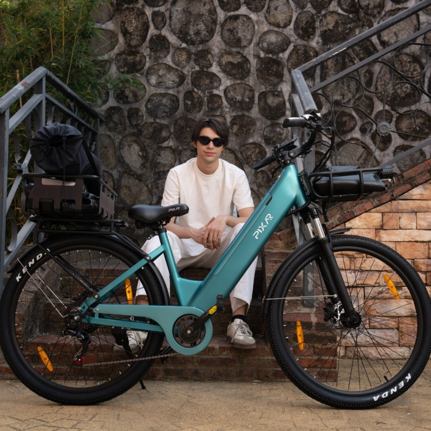 Mężczyzna w bieli siedzi na schodach obok turkusowego roweru elektrycznego.