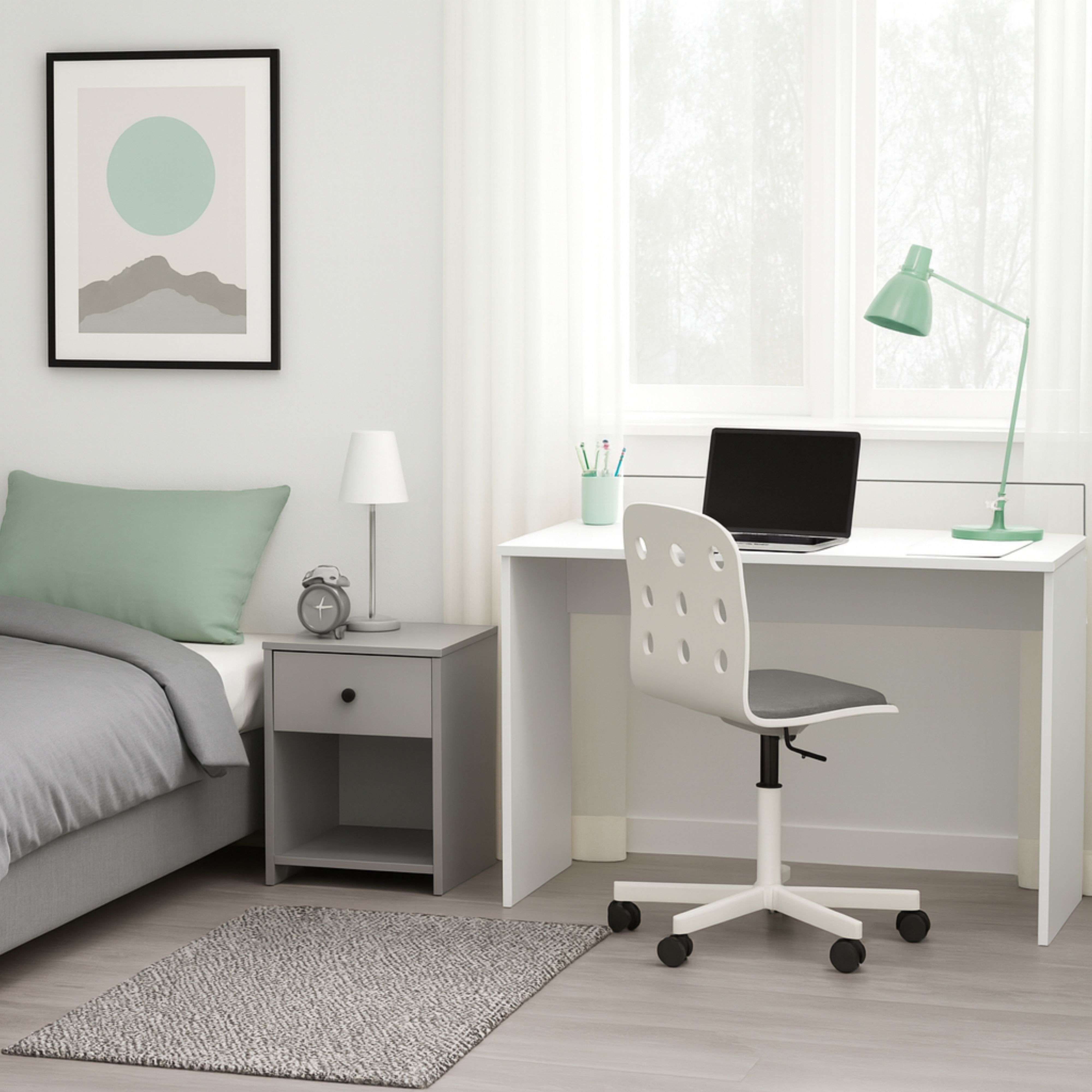 Un dormitorio ordenado con cama, escritorio, silla y mesita de noche.