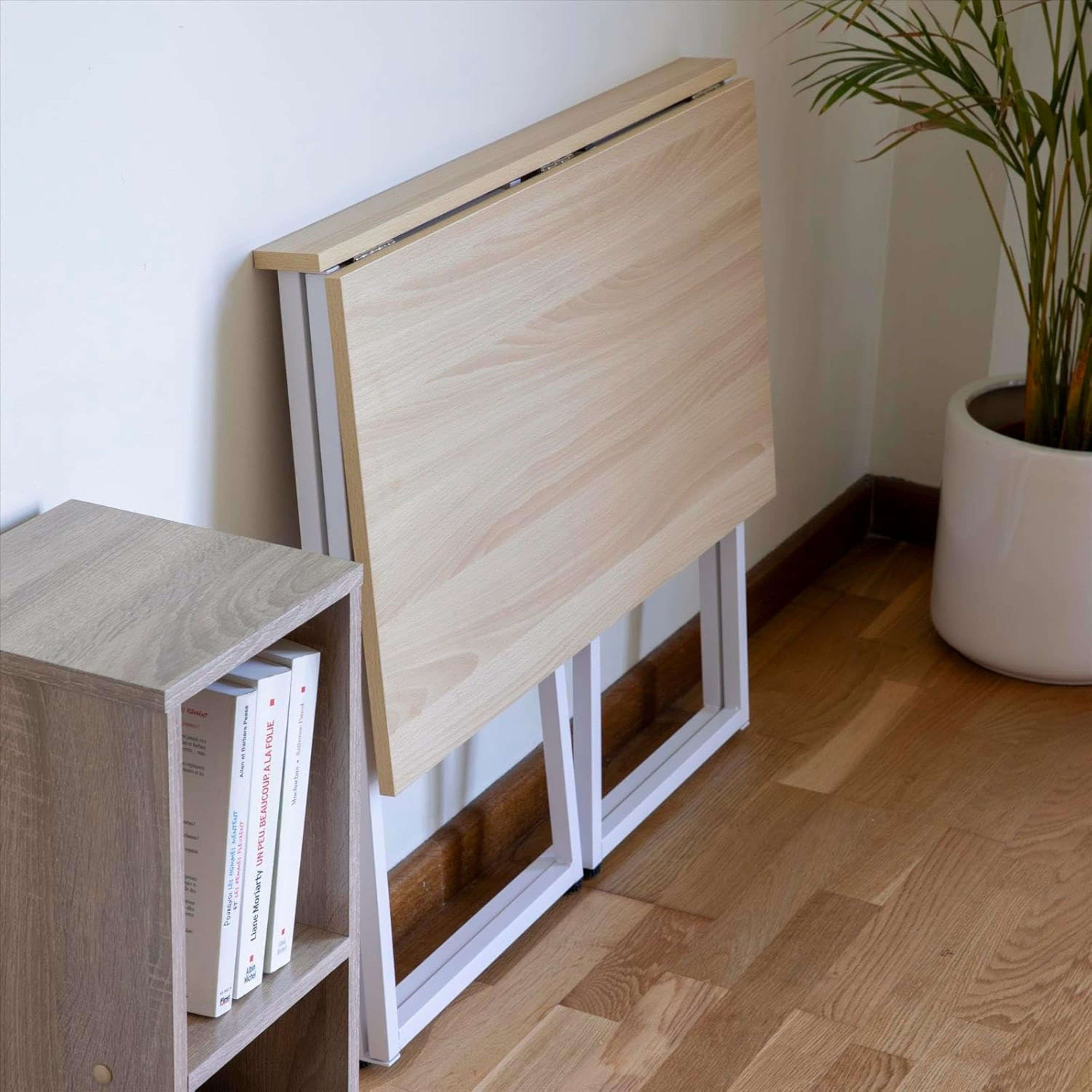 Una mesa plegable de madera clara junto a una estantería con libros y una planta.