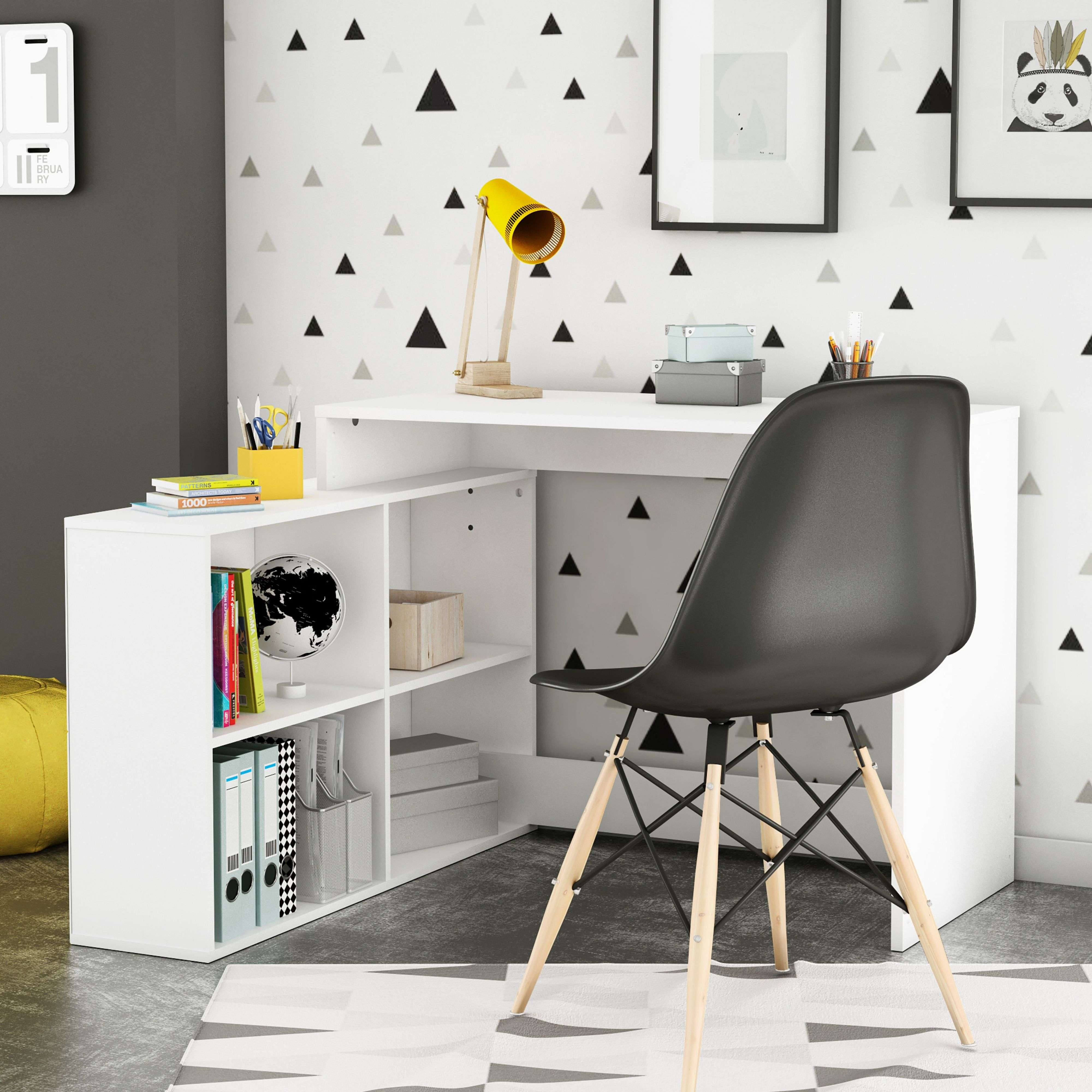 Un escritorio blanco con silla negra, libros, lámpara y decoración de pared.
