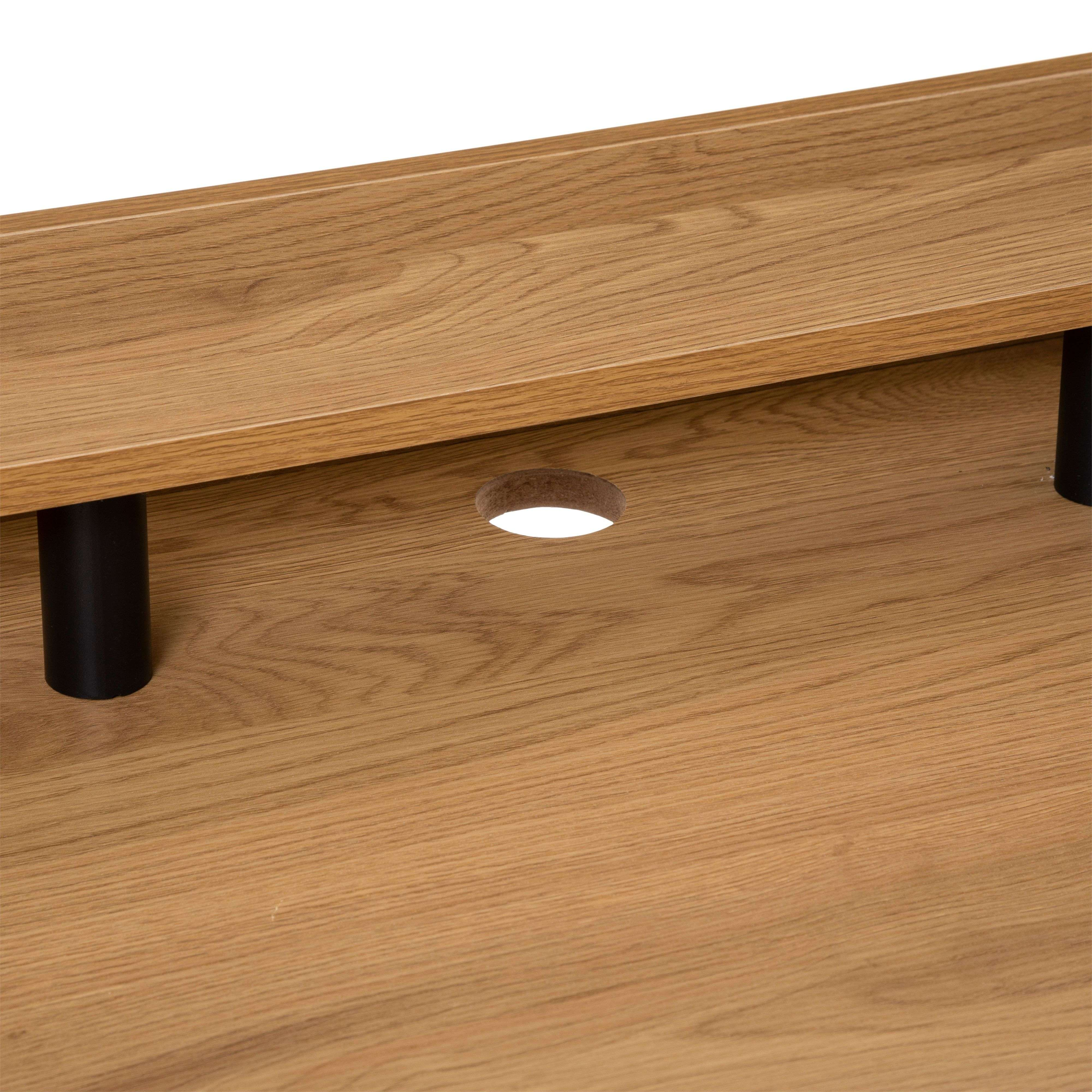 Primer plano de una mesa de madera con orificio para cables y patas negras.