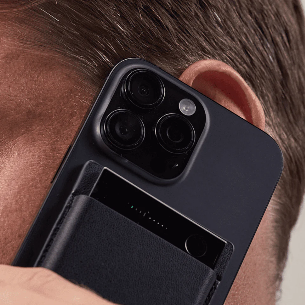 Zbliżenie na mężczyznę trzymającego przy uchu ciemny smartfon z etui na karty.