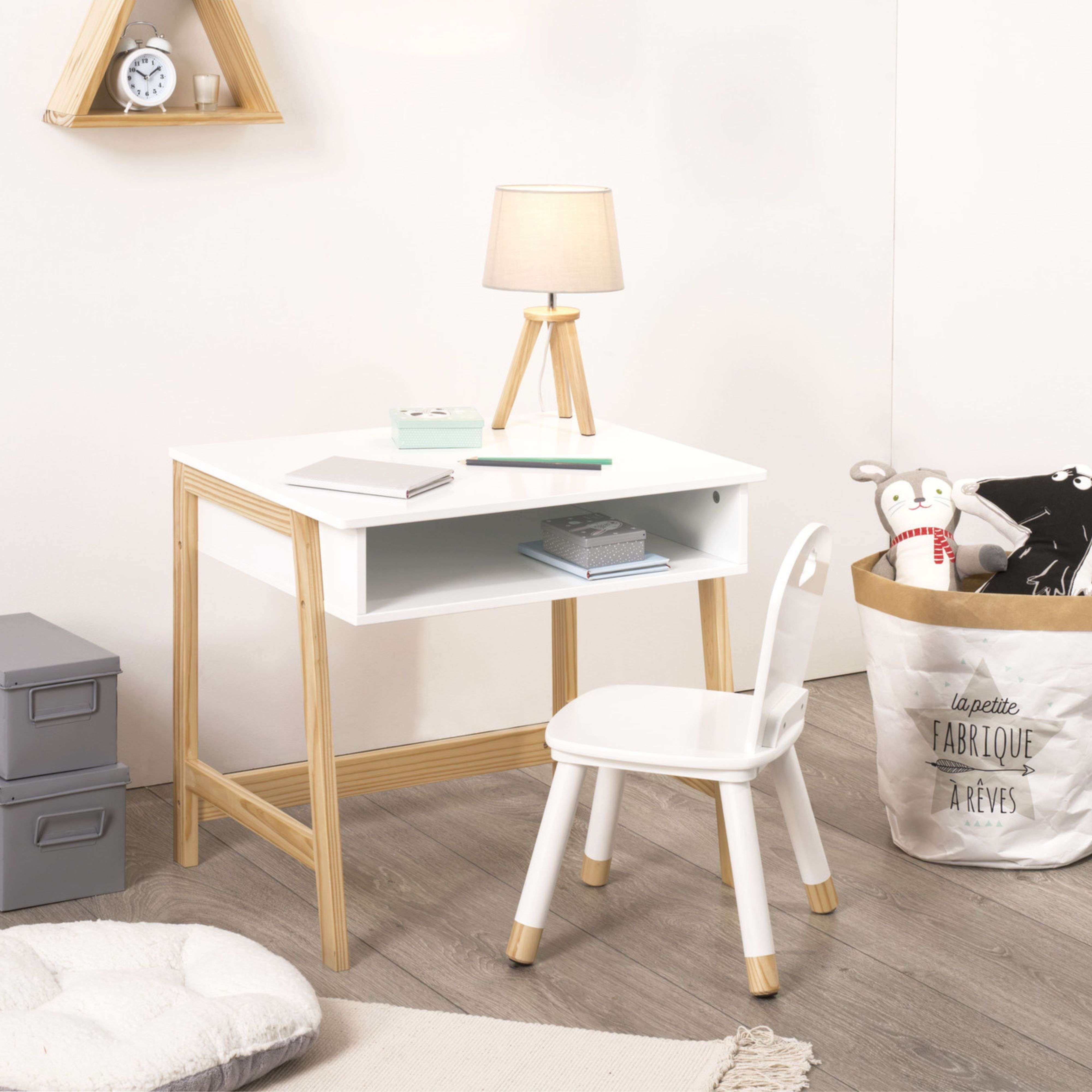 Un escritorio blanco con patas de madera, silla, lámpara y cesto de juguetes.