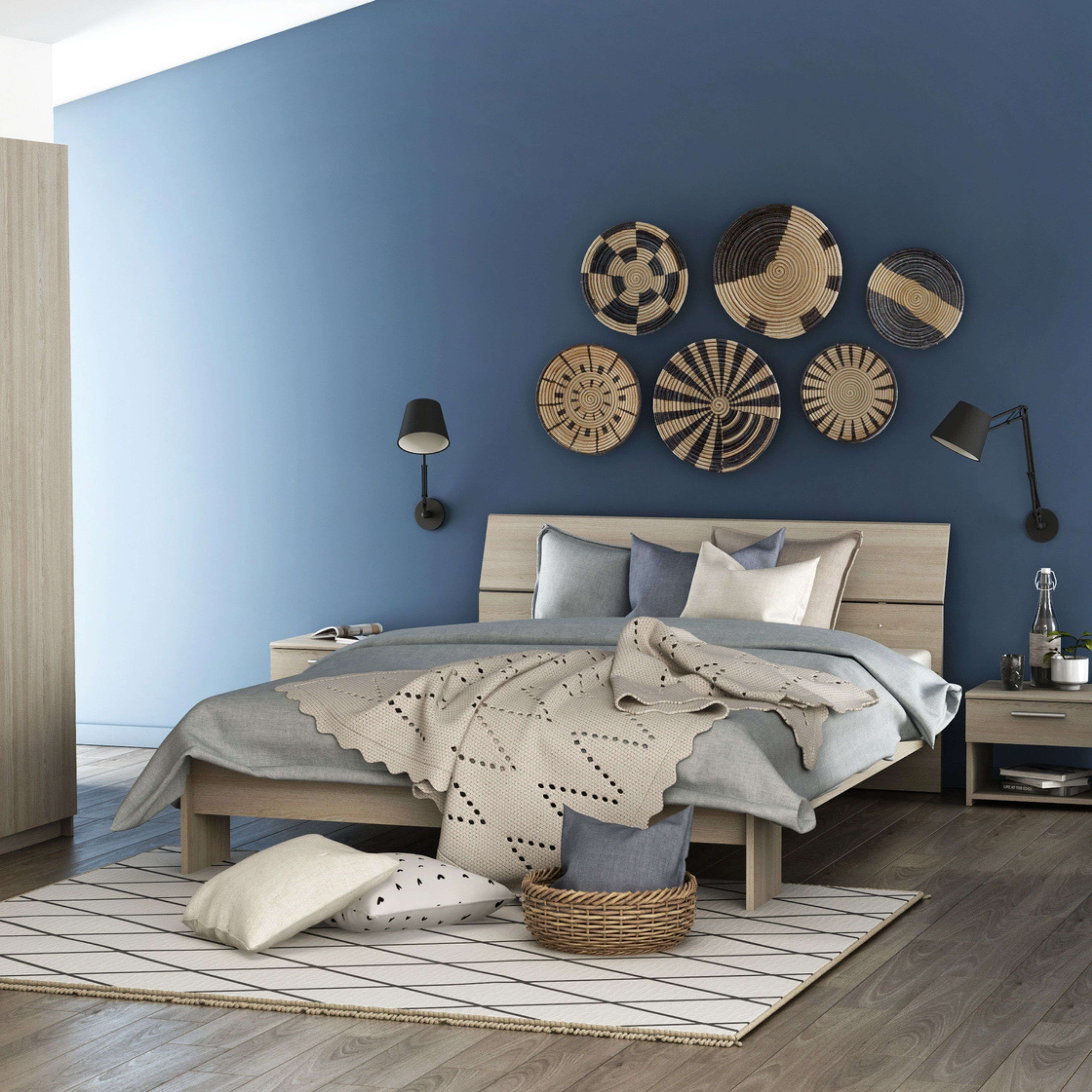 Un dormitorio con pared azul, cama de madera, manta y cestas de pared.