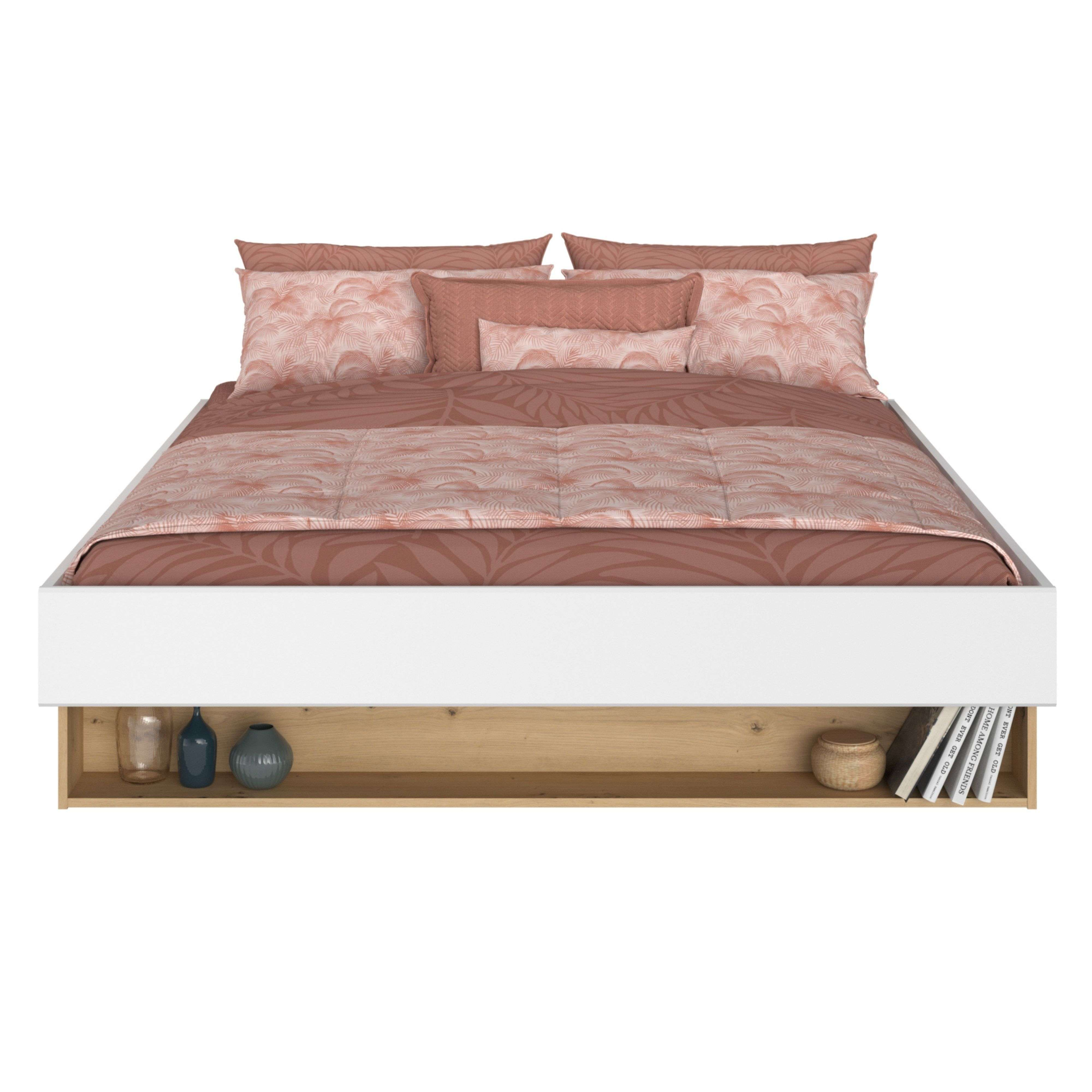 Una cama blanca con ropa de cama de hojas rosas y estante de madera con decor.