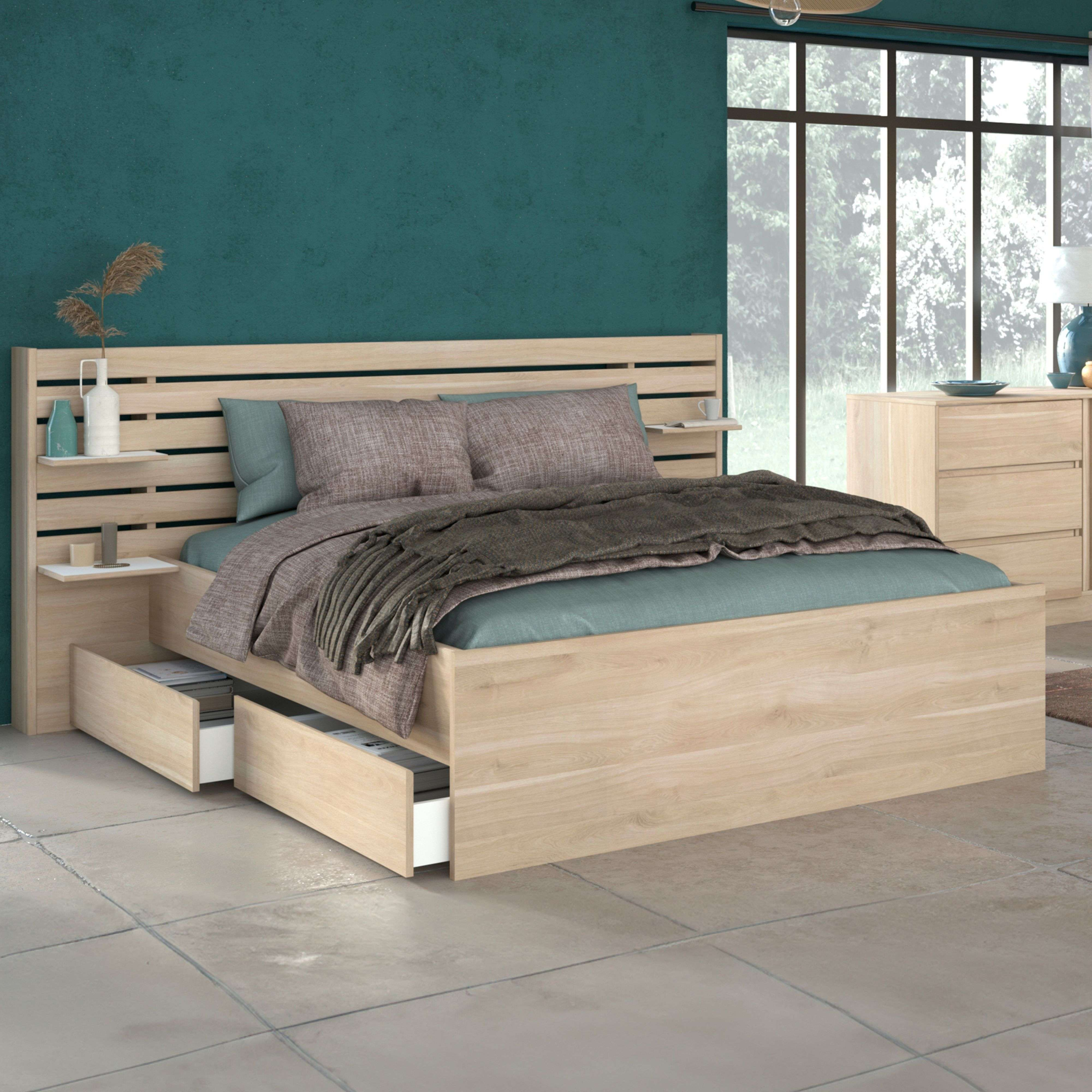 Una cama de madera clara con cajones, cojines y manta frente a una ventana grande.